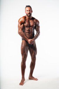 Bodybuilder posiert mit muskulösem Körper auf weißem Hintergrund für Fitness- und Trainingsinspiration.
