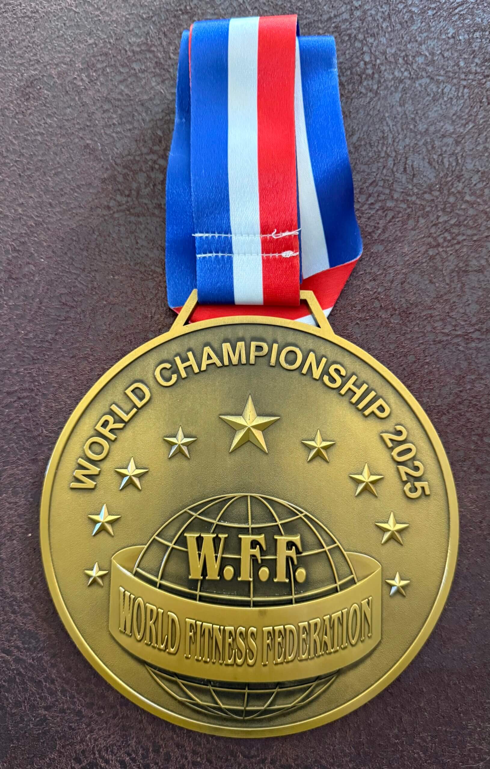 Goldmedaille der World Fitness Federation World Championship 2025 mit blau-weiß-rotem Band.