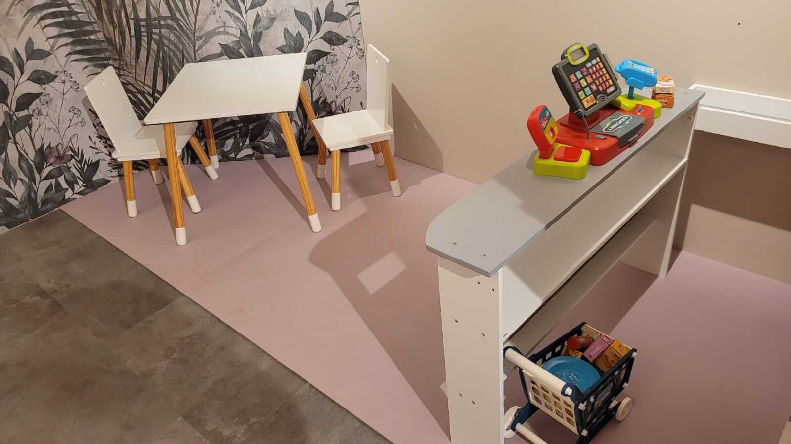 Kinderspielecke mit Tisch, Stühlen und Spielkasse, ideal für kreatives Lernen und Rollenspiele im Kinderzimmer.