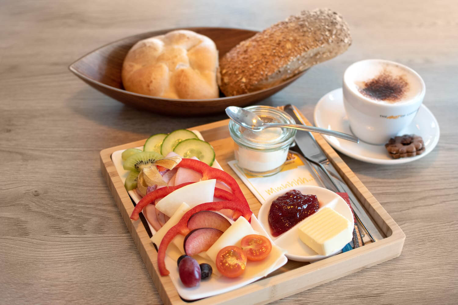 Frühstücksteller mit Brot, Aufschnitt, Käse, Obst, Joghurt und Kaffee für einen energiereichen Start in den Tag.
