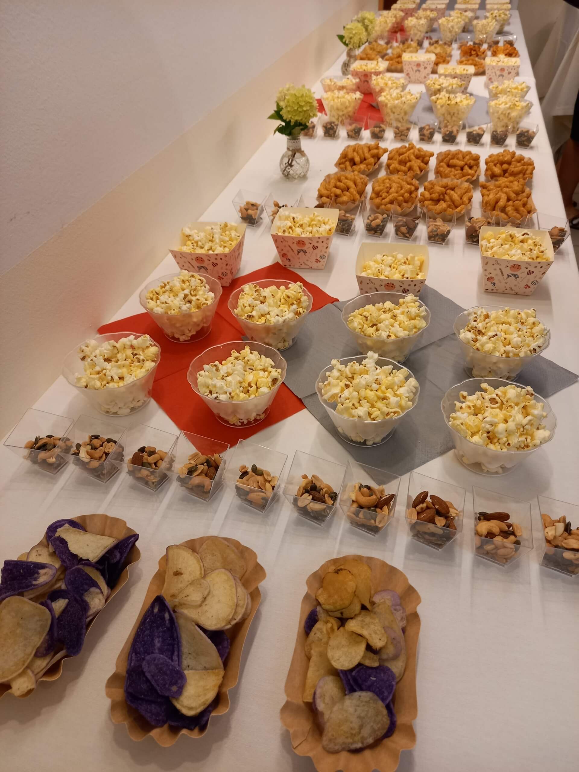 Vielfältiges Snack-Buffet mit Popcorn, Chips und Nüssen auf Tisch, ideal für Event oder Party.