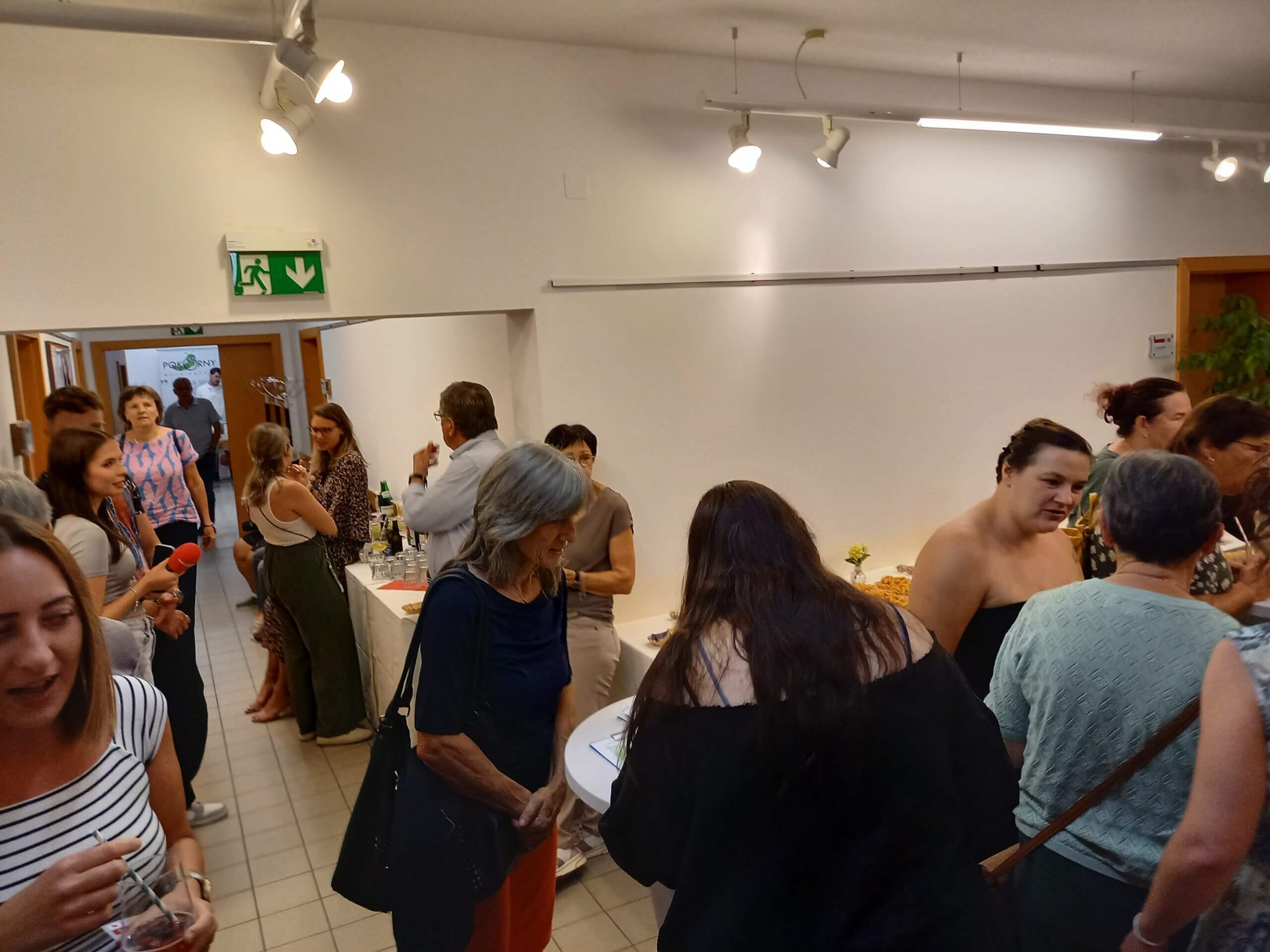 Personen bei einem geselligen Empfang in einem hellen Raum, Gespräche und Buffet im Hintergrund.