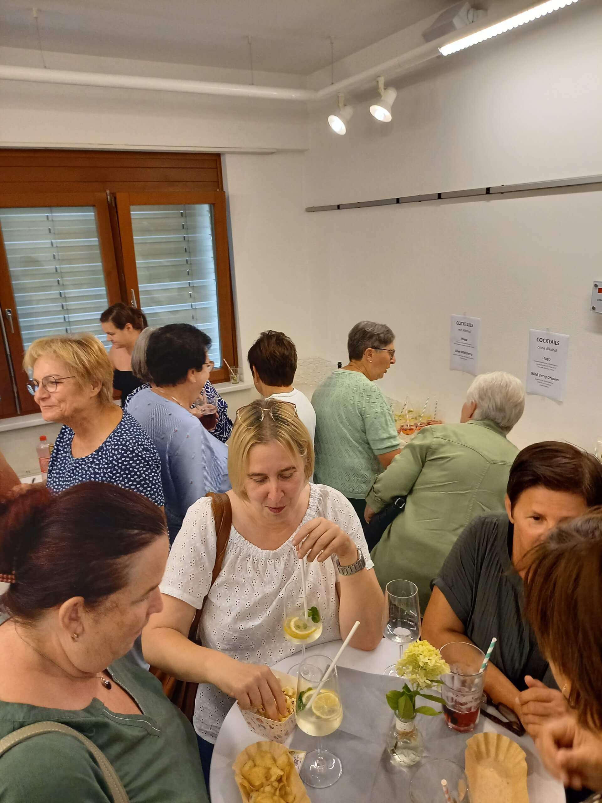 Gruppe von Frauen genießt Cocktails und Snacks bei einer geselligen Veranstaltung in einem modernen Raum.
