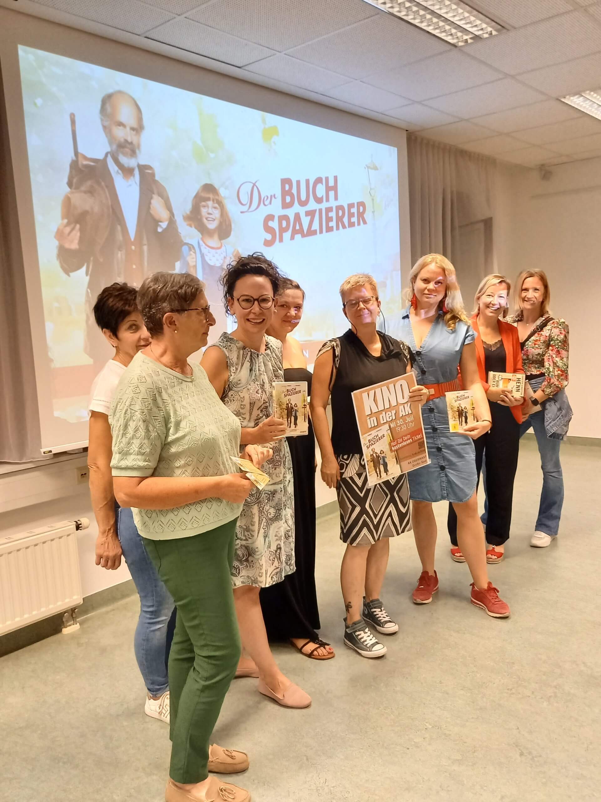 Personen präsentieren Bücher bei einer Veranstaltung zu Der Buchspazierer mit Filmposter im Hintergrund.