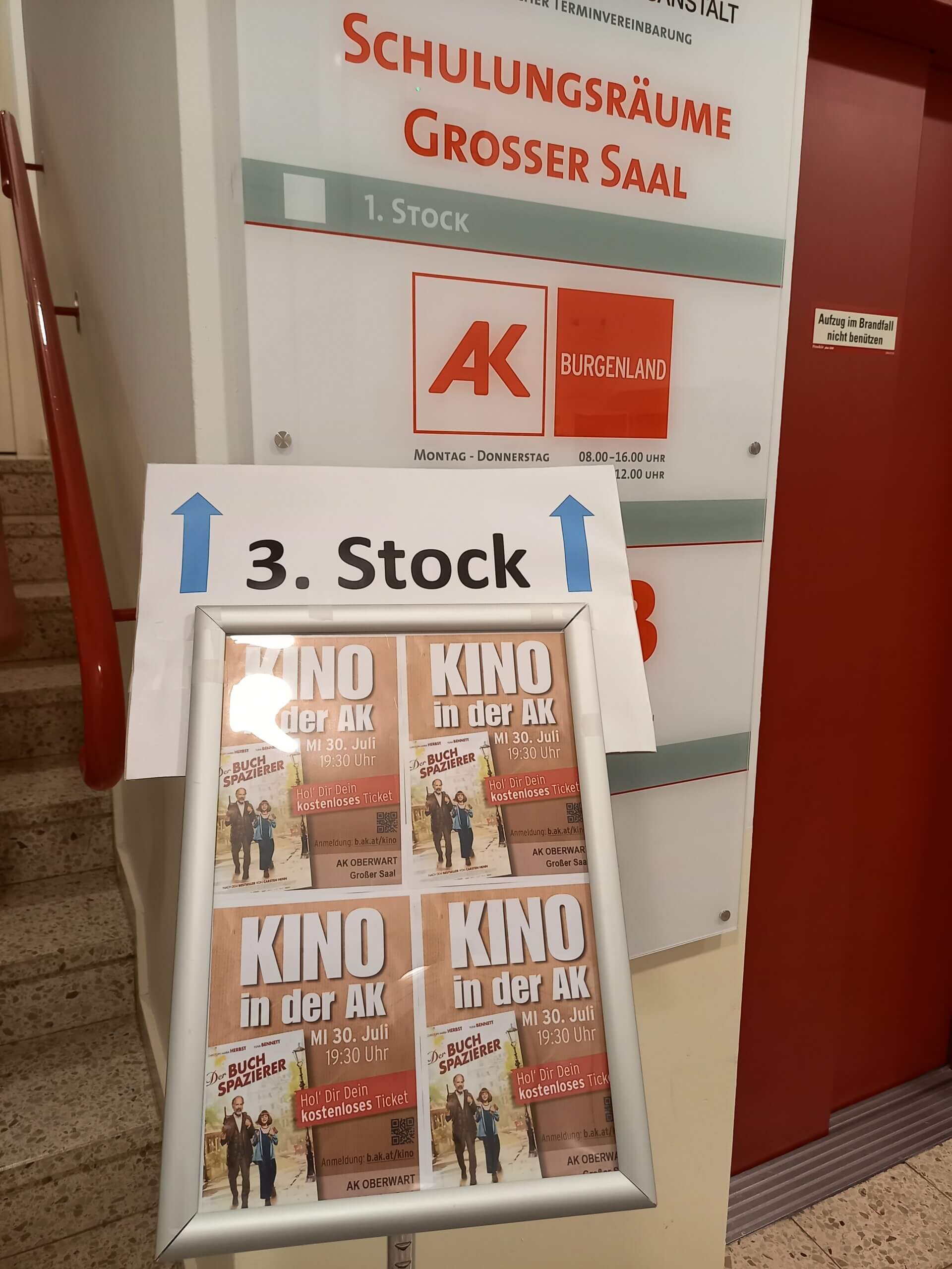 Wegweiser zur Arbeiterkammer Oberwart mit Kinohinweis am 3. Stock; Plakate für Kino in der AK am 30. Juli.