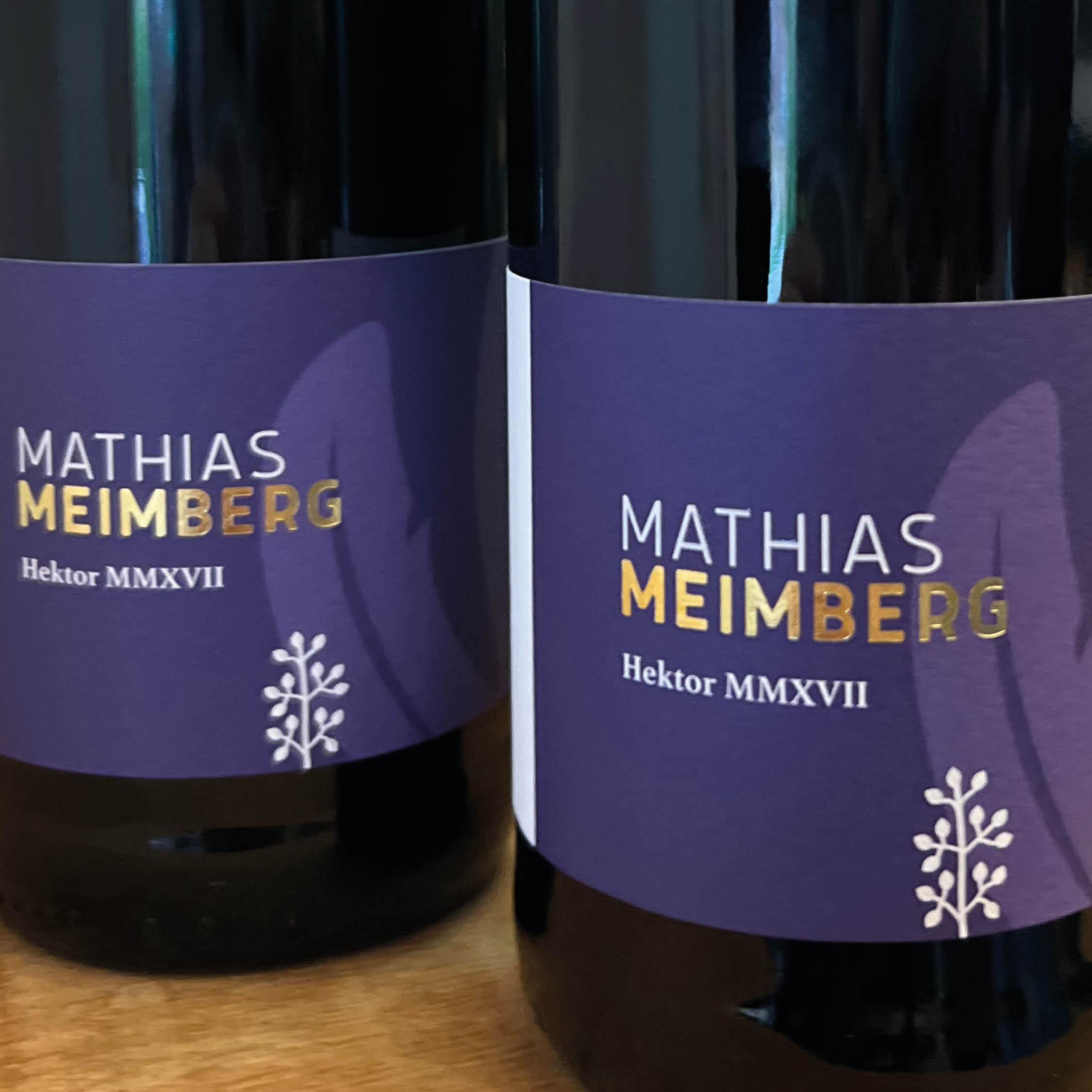 Zwei Weinflaschen mit lila Etikett von Mathias Meimberg Hektor MMXVII auf Holztisch.