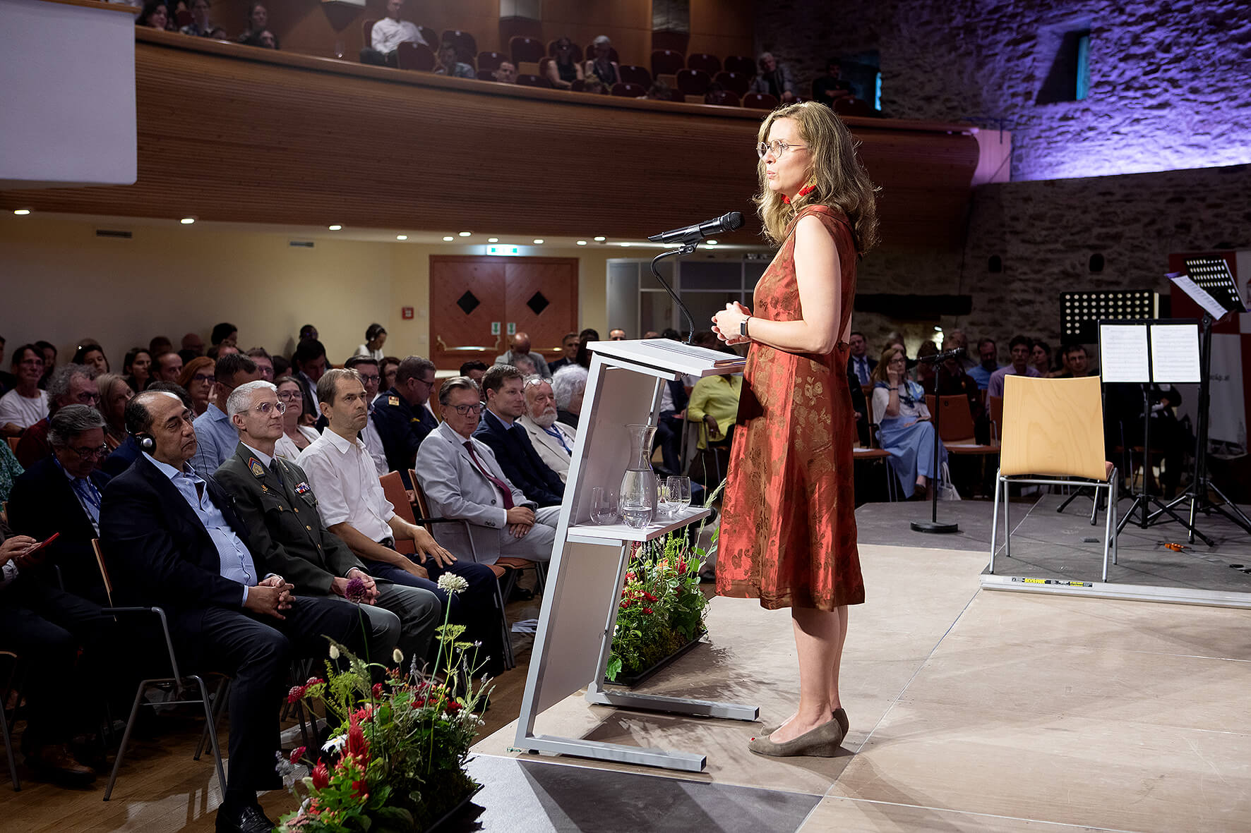 Frau hält Rede auf Bühne vor interessiertem Publikum in einem Konferenzsaal.