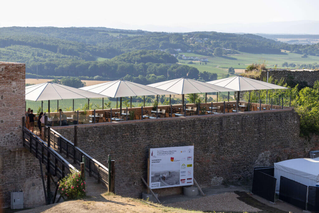 @foto muik 786682 Terrasse mit Sonnenschirmen und Blick auf grüne Hügel; einladender Ort zum Entspannen in historischer Umgebung.
