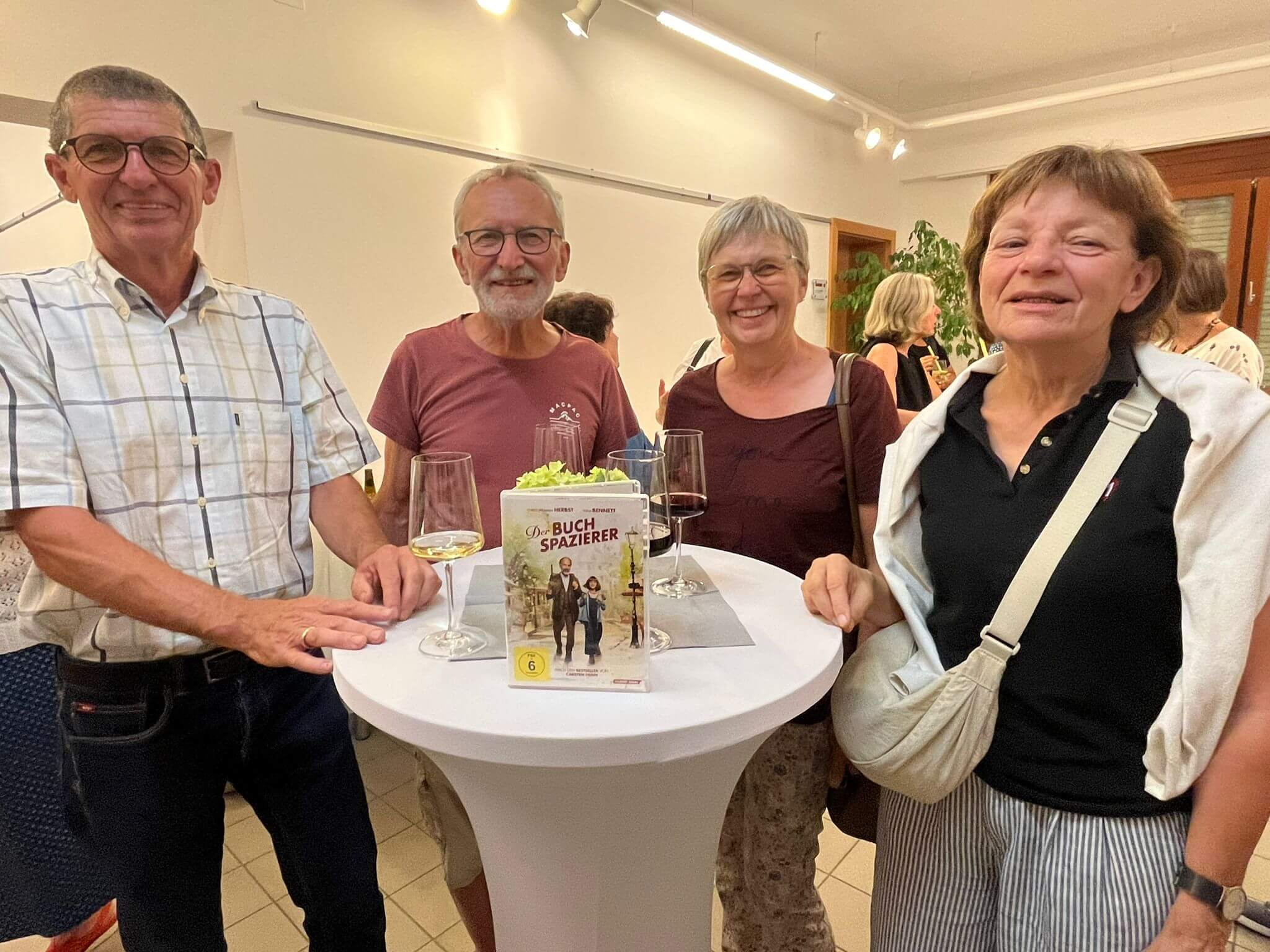 Gruppe von Menschen bei einer Buchpräsentation mit Getränken in einem hell erleuchteten Raum.
