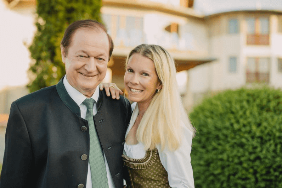 Larimar Johann Haberl und Daniela Lakosche©Hotel Larimar Mann und Frau in traditioneller bayerischer Tracht lächeln vor einem modernen Gebäude in die Kamera.