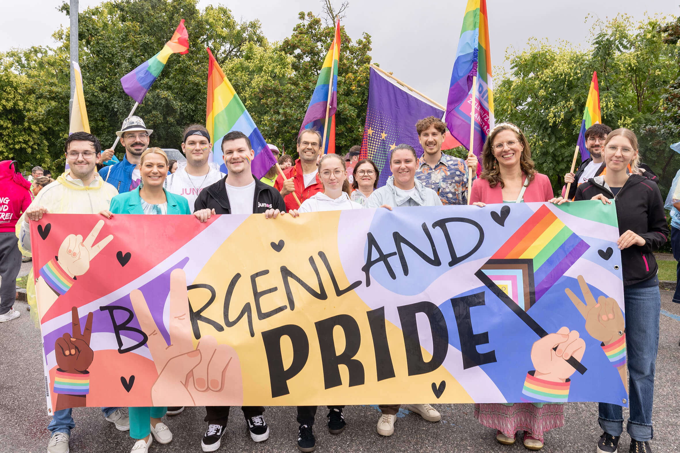 Personengruppe mit Burgenland Pride-Banner und Regenbogenflaggen, feiert Vielfalt und Inklusion bei einer Outdoor-Veranstaltung.