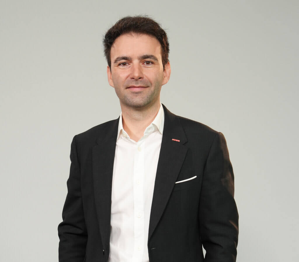 michael-nemeth Mann in Anzug vor grauem Hintergrund, lächelnd und zuversichtlich, porträtiert in einem professionellen Setting.