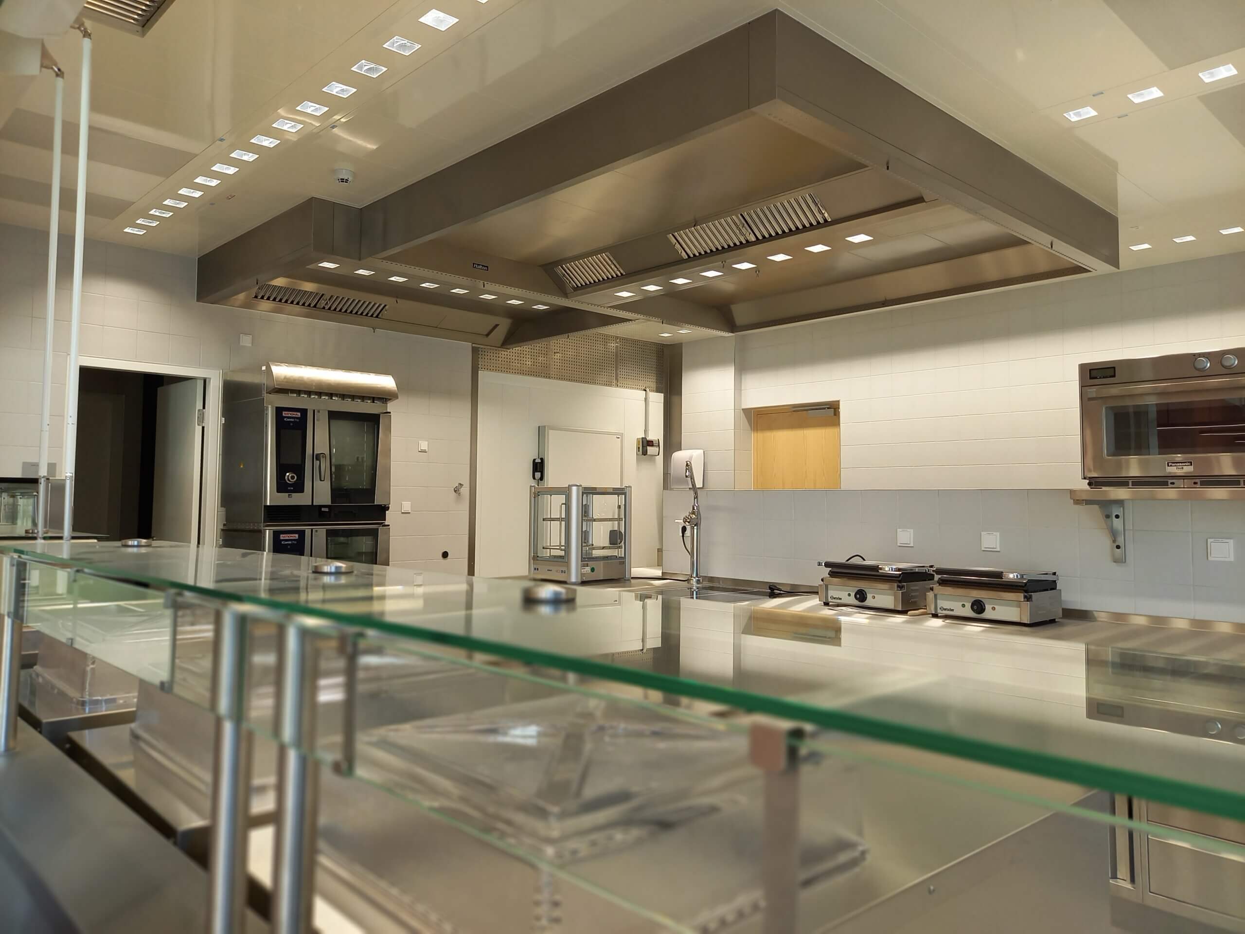 Moderne Profiküche mit Edelstahlgeräten, Belüftung und Glasabdeckung. Optimal für gastronomische Betriebe.