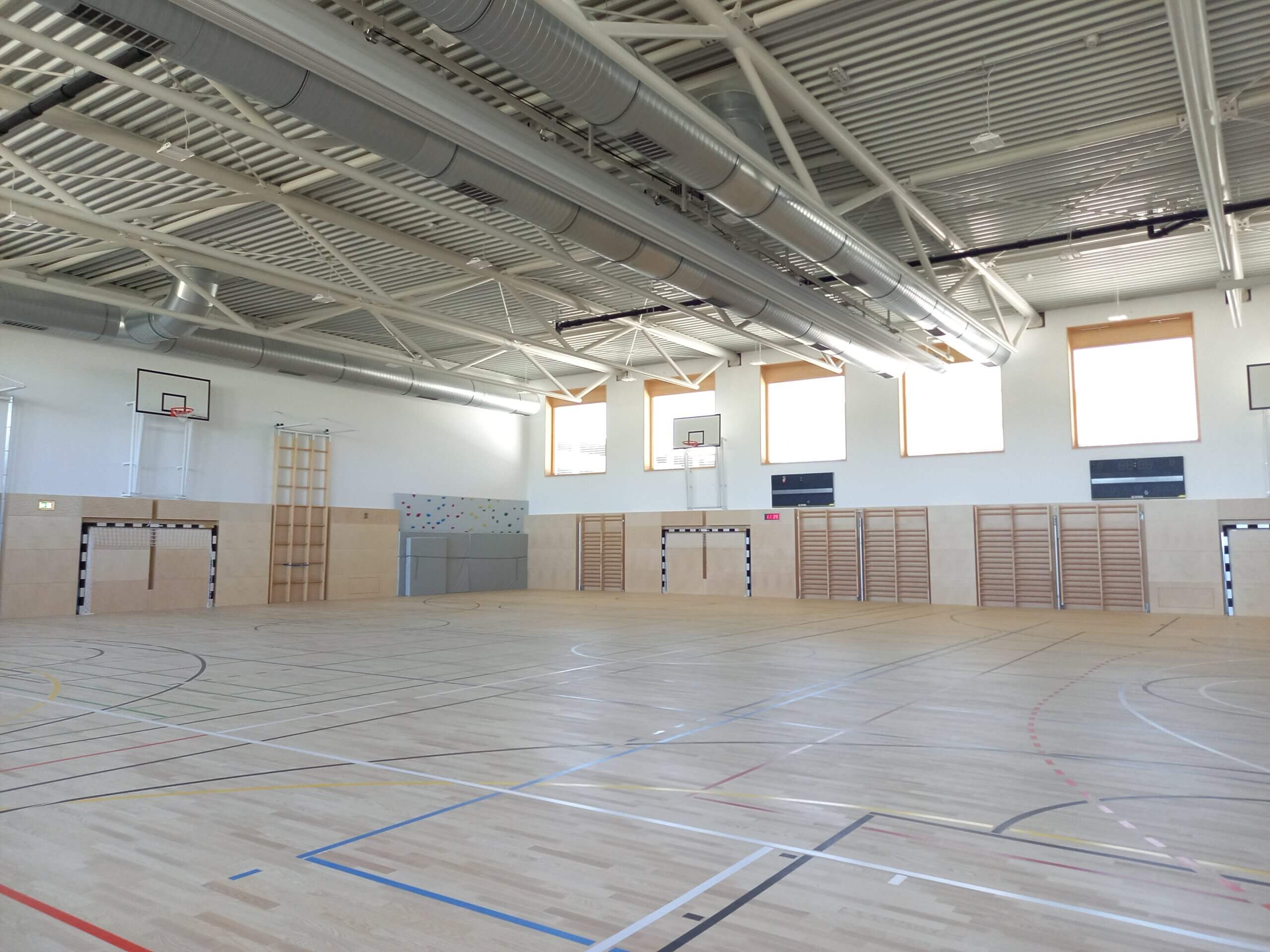 Moderne Sporthalle mit Basketballkörben und Kletterwand, ideal für Indoor-Sportarten und Schulsportaktivitäten.
