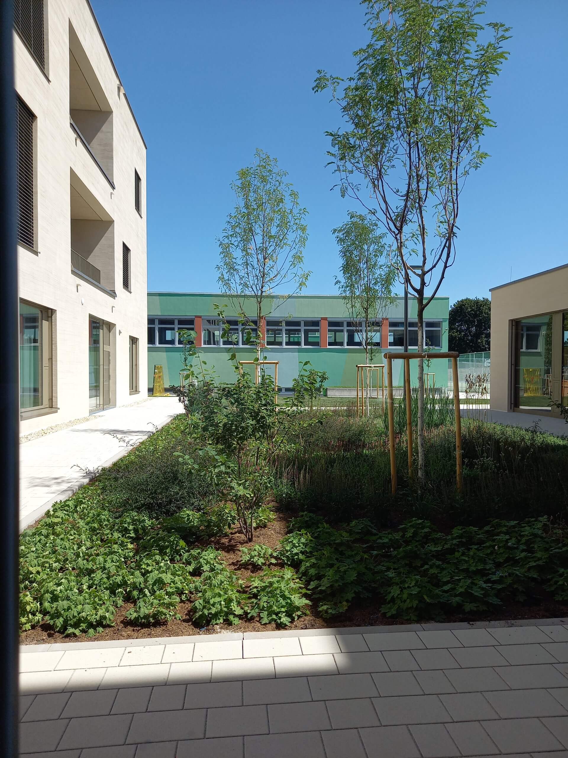Moderner Innenhof mit angelegtem Garten, von Gebäuden umgeben, unter strahlend blauem Himmel.