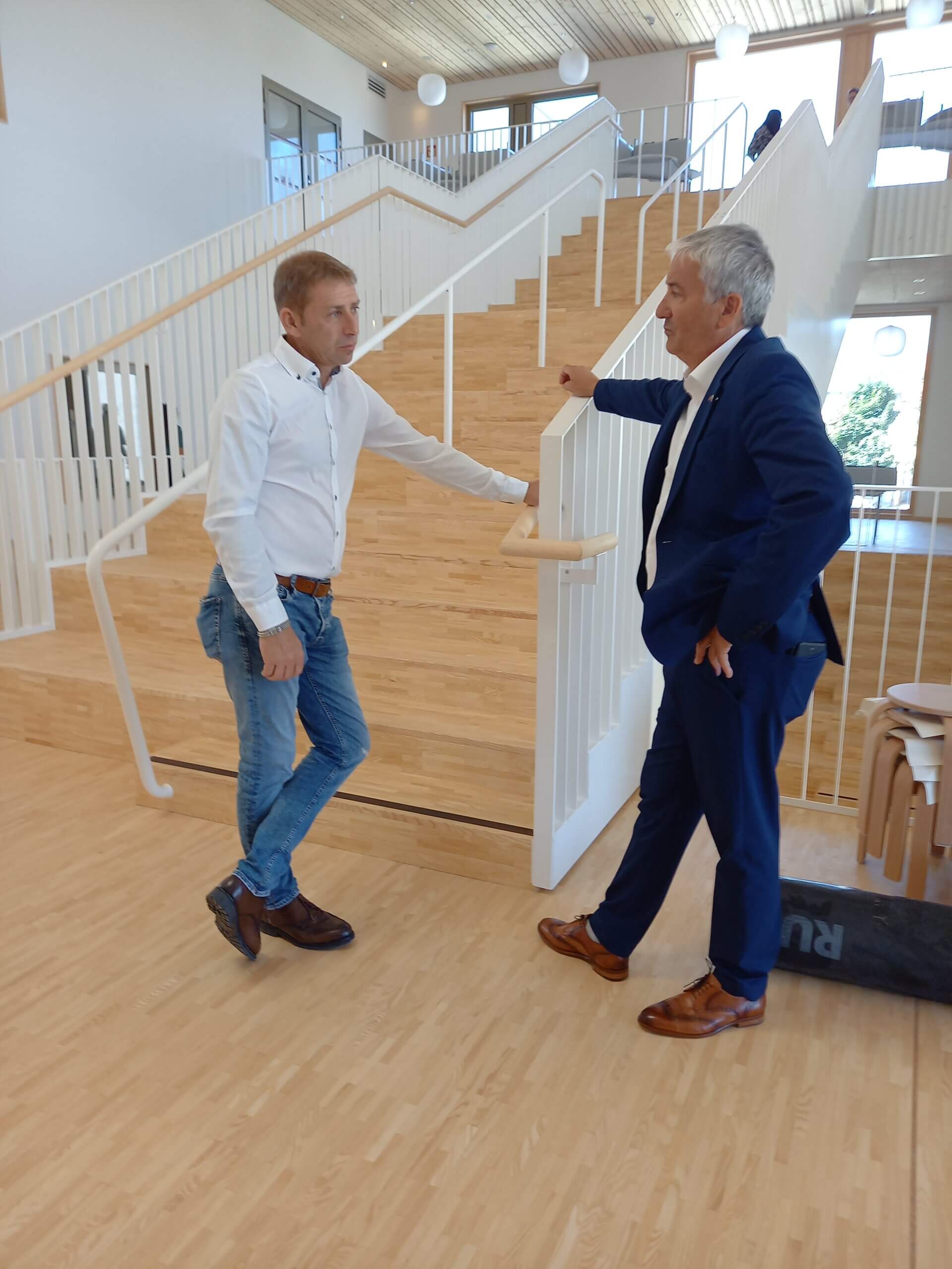 Zwei Männer im Business-Gespräch auf einer hellen Holztreppe, moderner Büro-Innenraum.