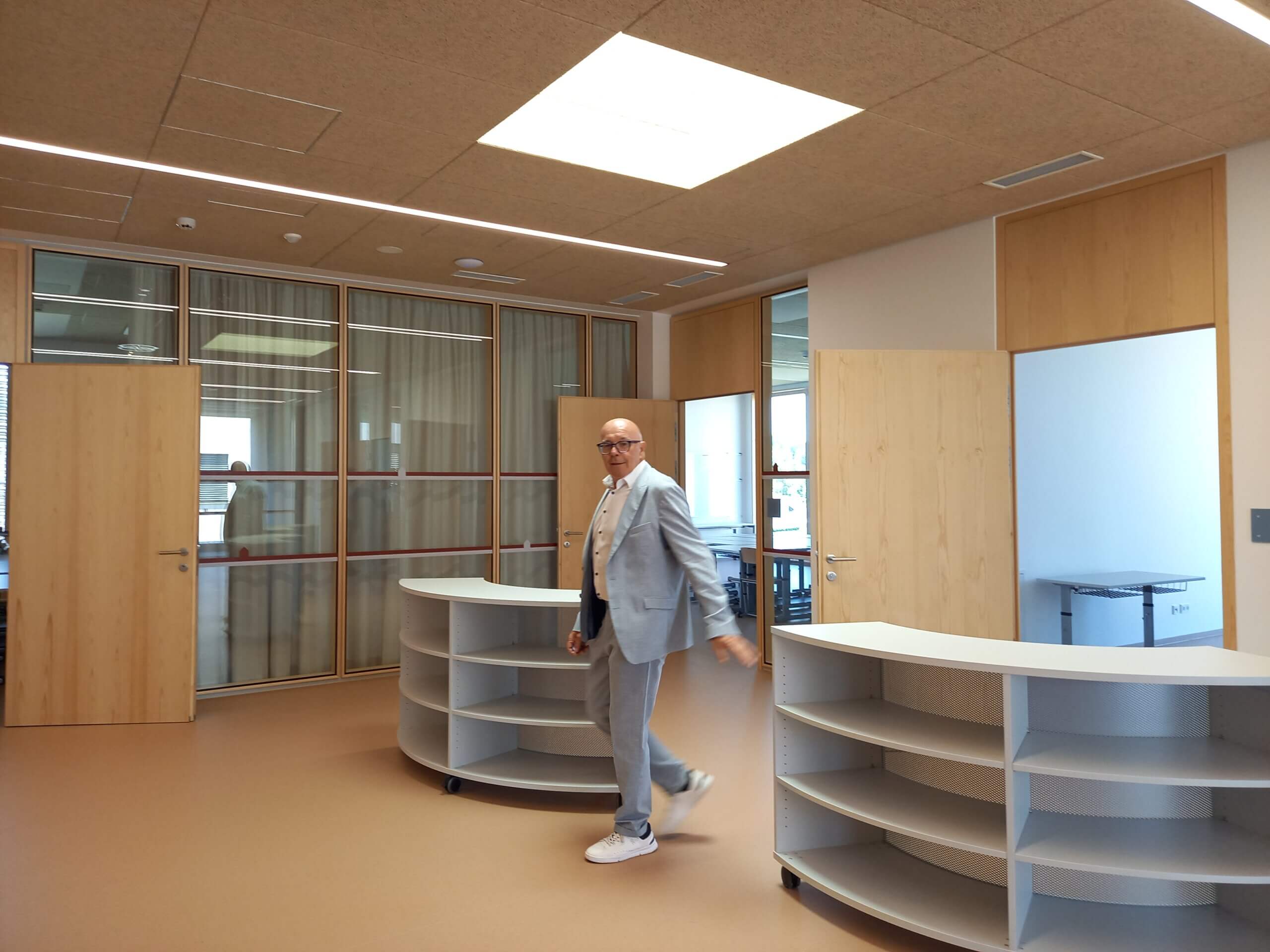 Mann in modernem Büro mit Holz- und Glastüren, lächelt und bewegt sich durch den Raum.