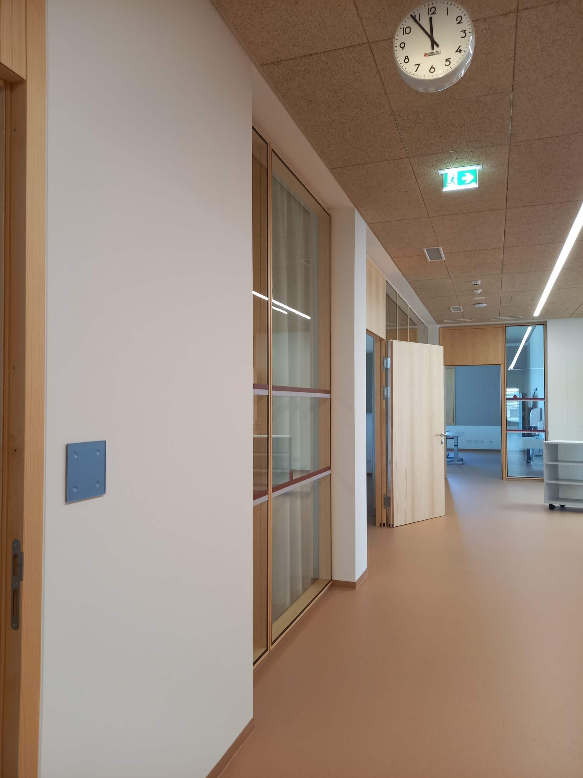 Moderner Büroraum mit hellen Holzdetails und Uhr an der Decke, zeigt minimalistisches Design und klare Linien.