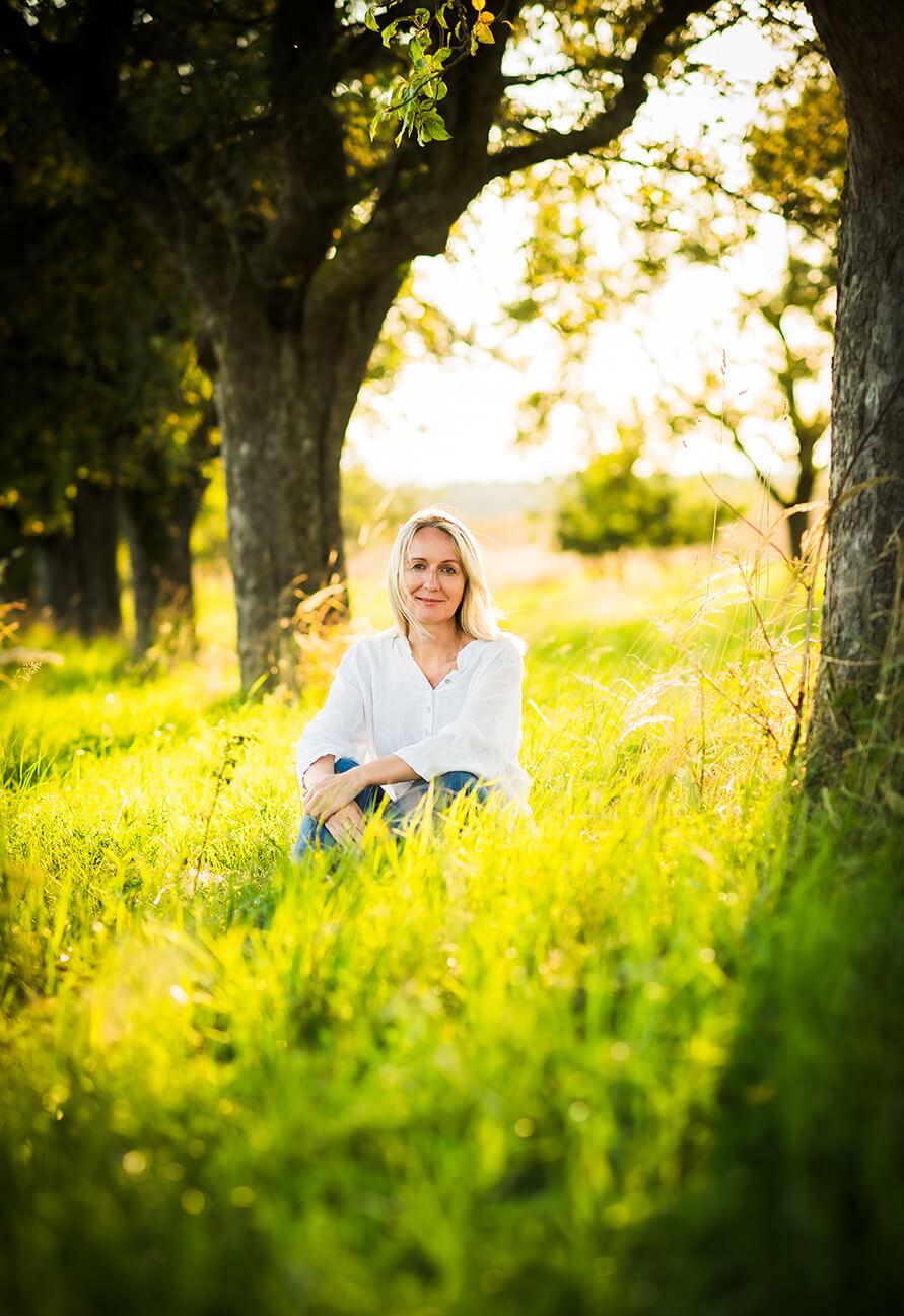 Frau sitzt entspannt auf einer grünen Wiese unter Bäumen, sonniger Tag, Naturgenuss, Erholung im Freien.