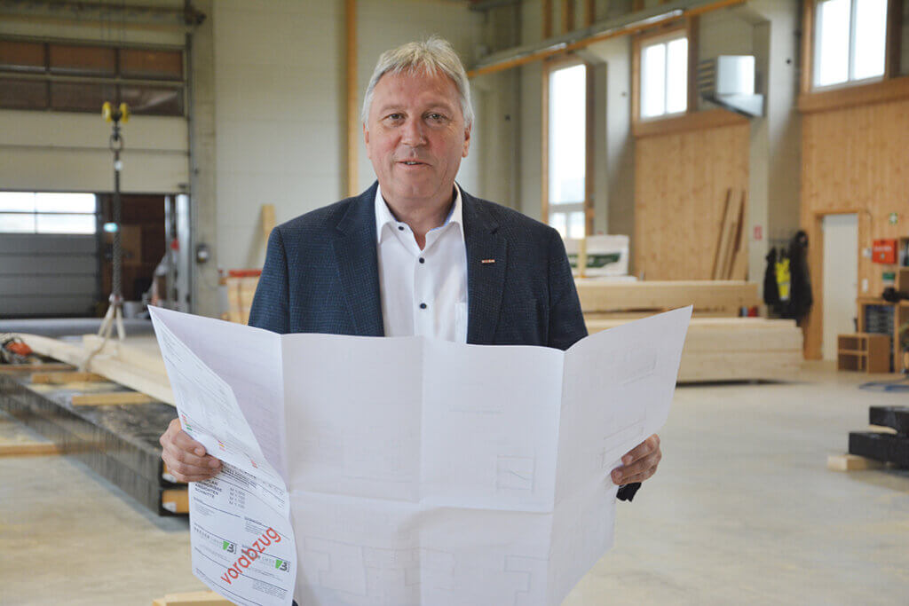 Eine Person in einer Werkstatt, die Baupläne hält, industrielles Umfeld im Hintergrund.