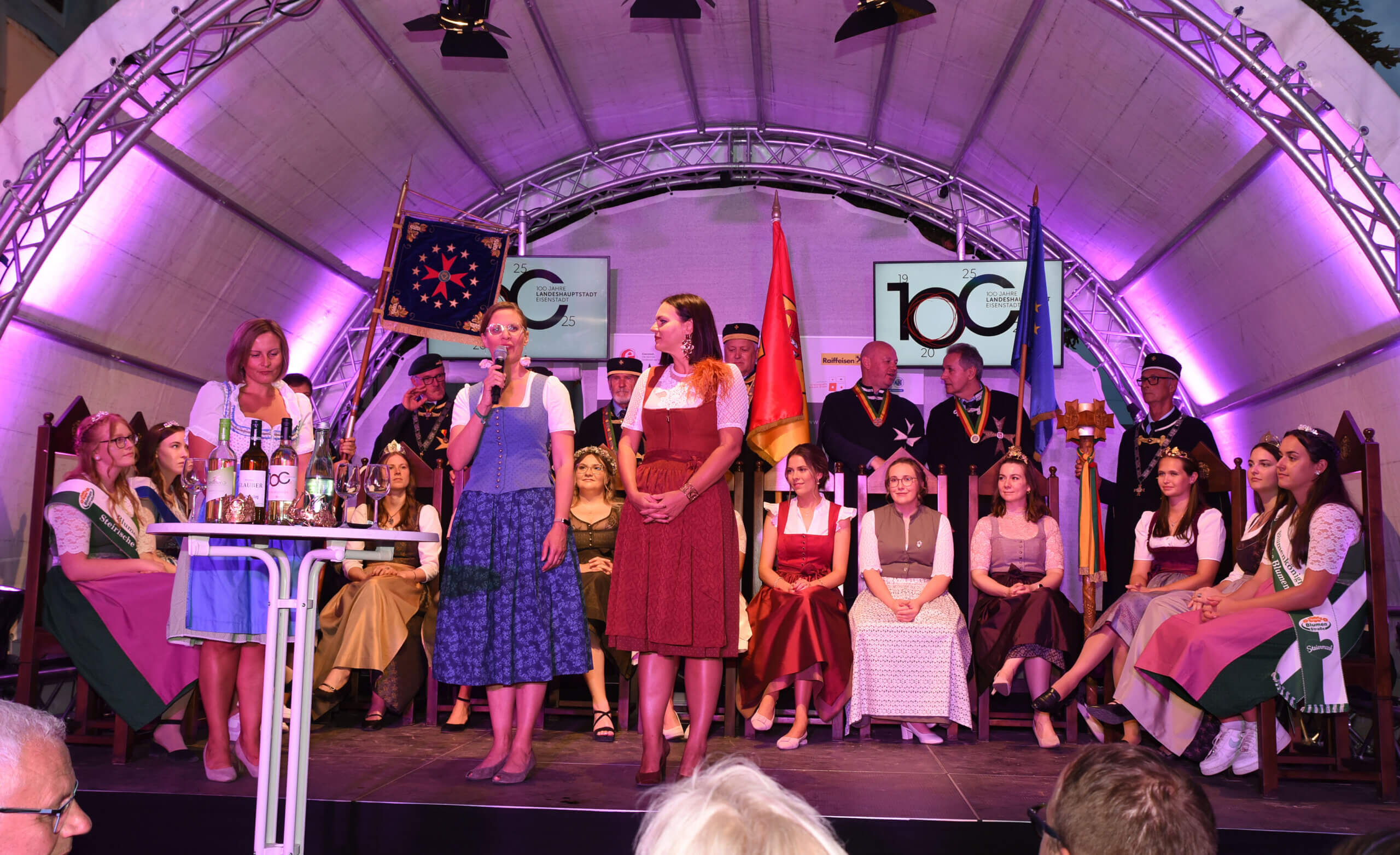 Festliche Feier mit traditionell gekleideten Personen bei einer Veranstaltung in einer dekorierten Festzeltbühne.