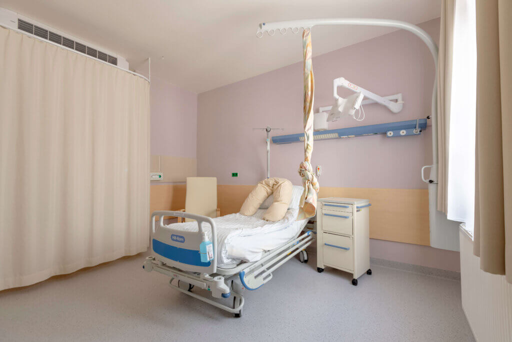 Modernes Krankenhauszimmer mit Bett, Infusionsständer und hellen Vorhängen für patientenfreundliche Pflegeumgebung.