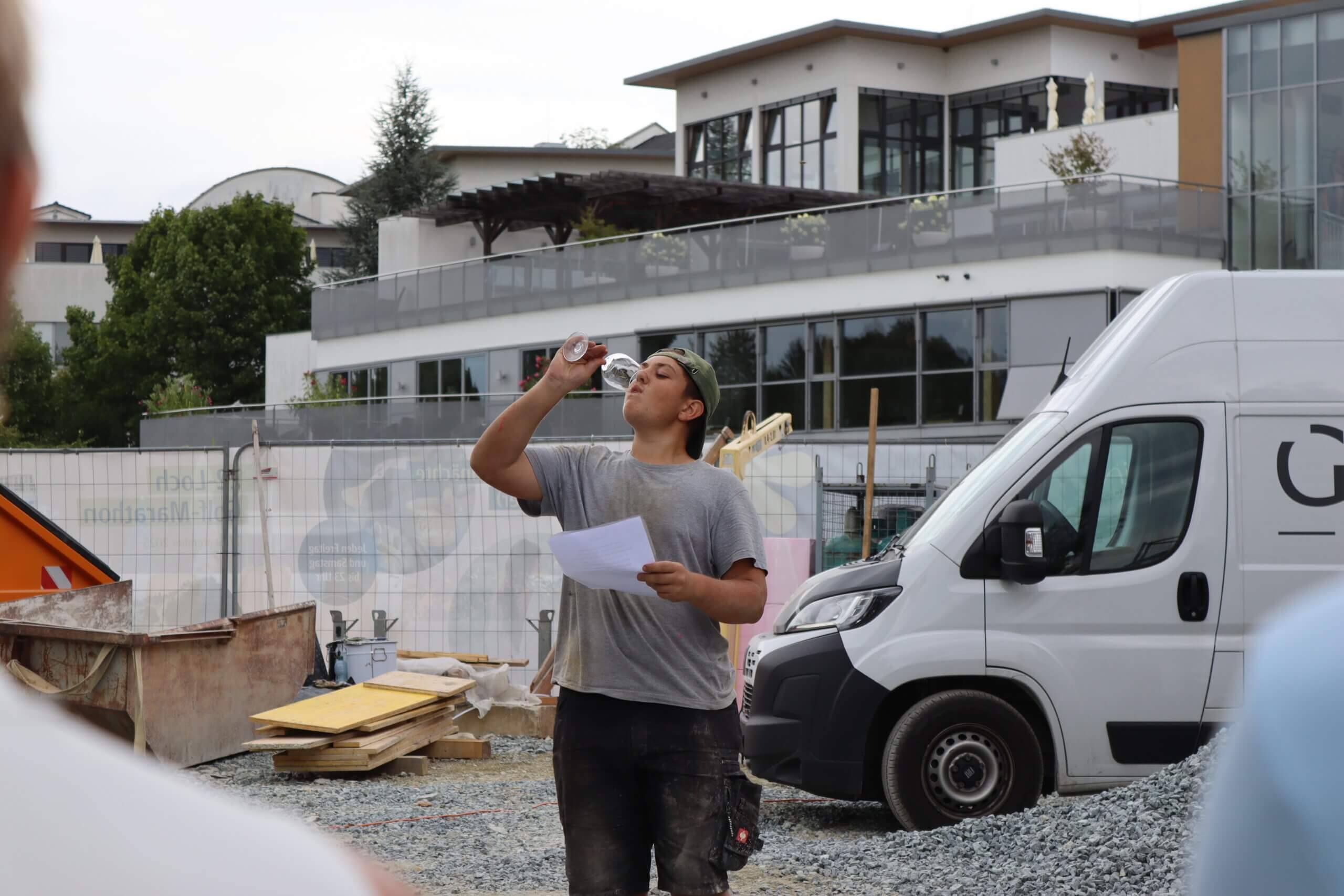 Bauarbeiter nimmt eine Pause, trinkt Wasser und hält Papiere auf einer Baustelle neben einem weißen Lieferwagen.
