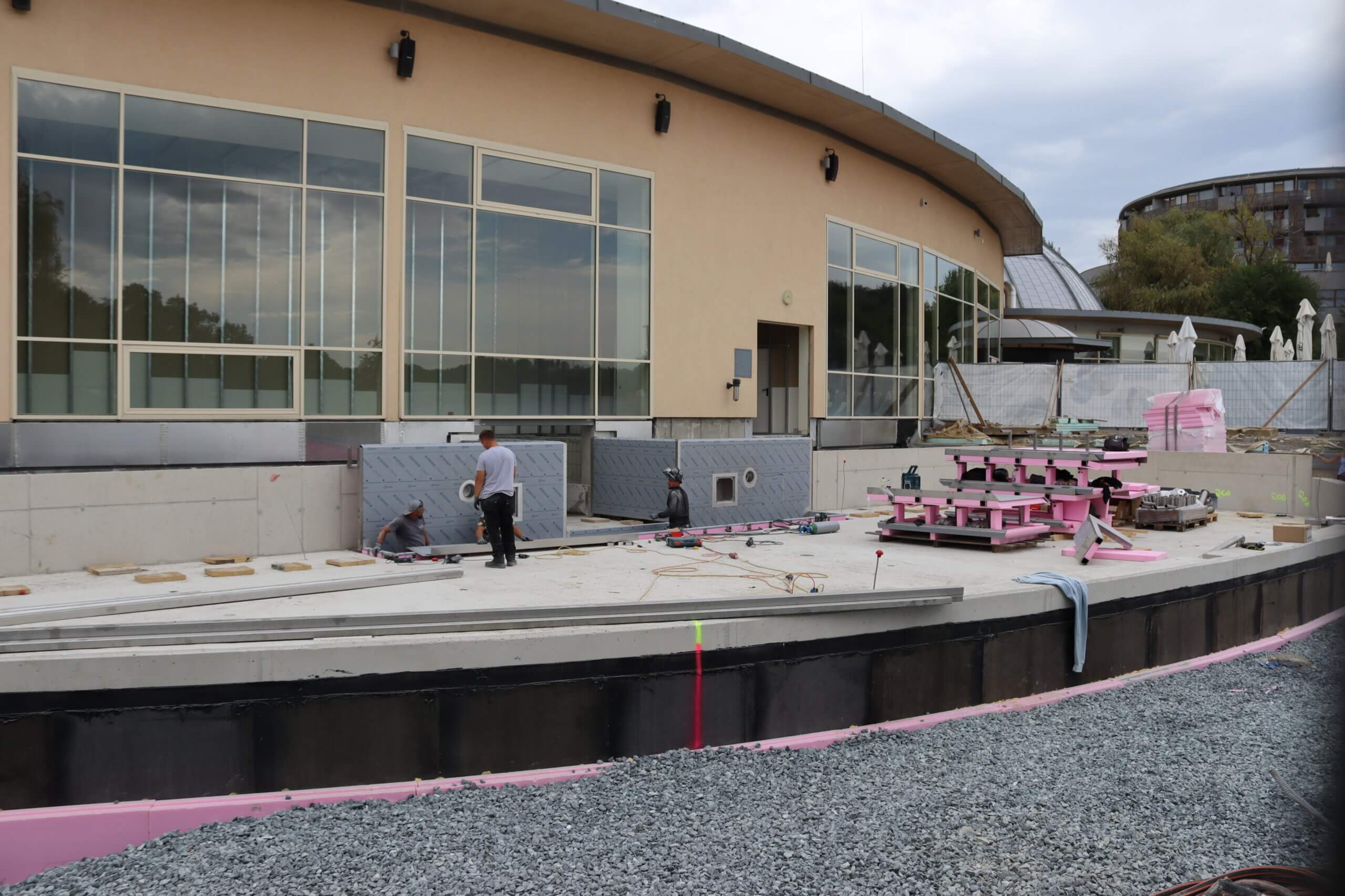 Arbeiter auf einer Baustelle mit großen Fenstern und moderner Architektur im Hintergrund. Neugestaltung im Gange.