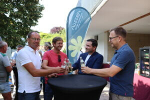 Vier Männer stoßen bei einer Veranstaltung im Freien an, Banner des Allegria Resorts im Hintergrund.