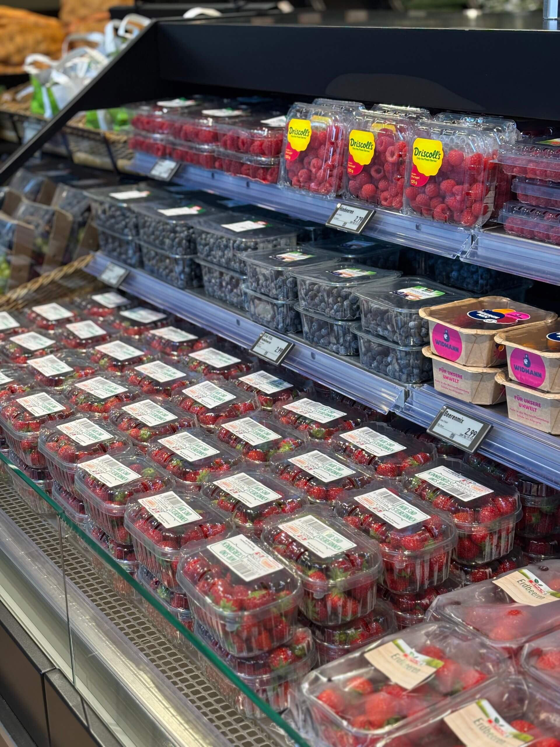 Frische Beeren im Supermarkt: Erdbeeren, Himbeeren und Blaubeeren in Plastikverpackungen, bereit zum Kauf.