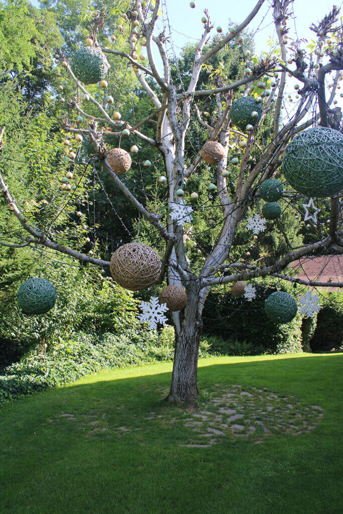 Baum mit dekorativen Kugeln und Schneeflocken im Garten, ideal für kreative Gartengestaltung im Sommer.