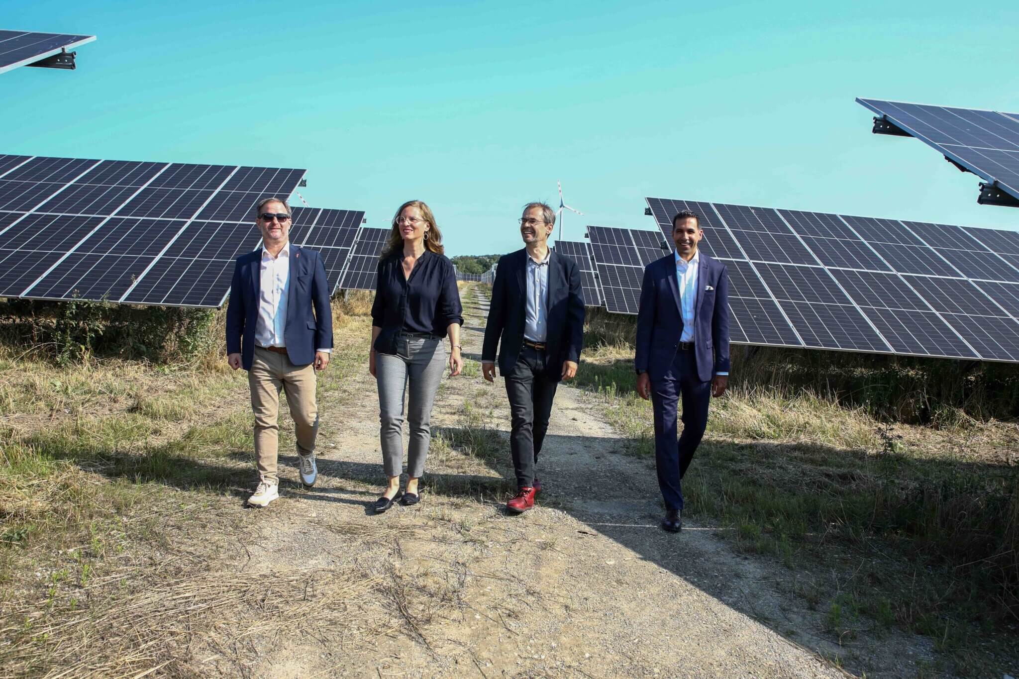 Gruppe von Menschen in Business-Kleidung geht durch ein Solarfeld bei sonnigem Wetter.