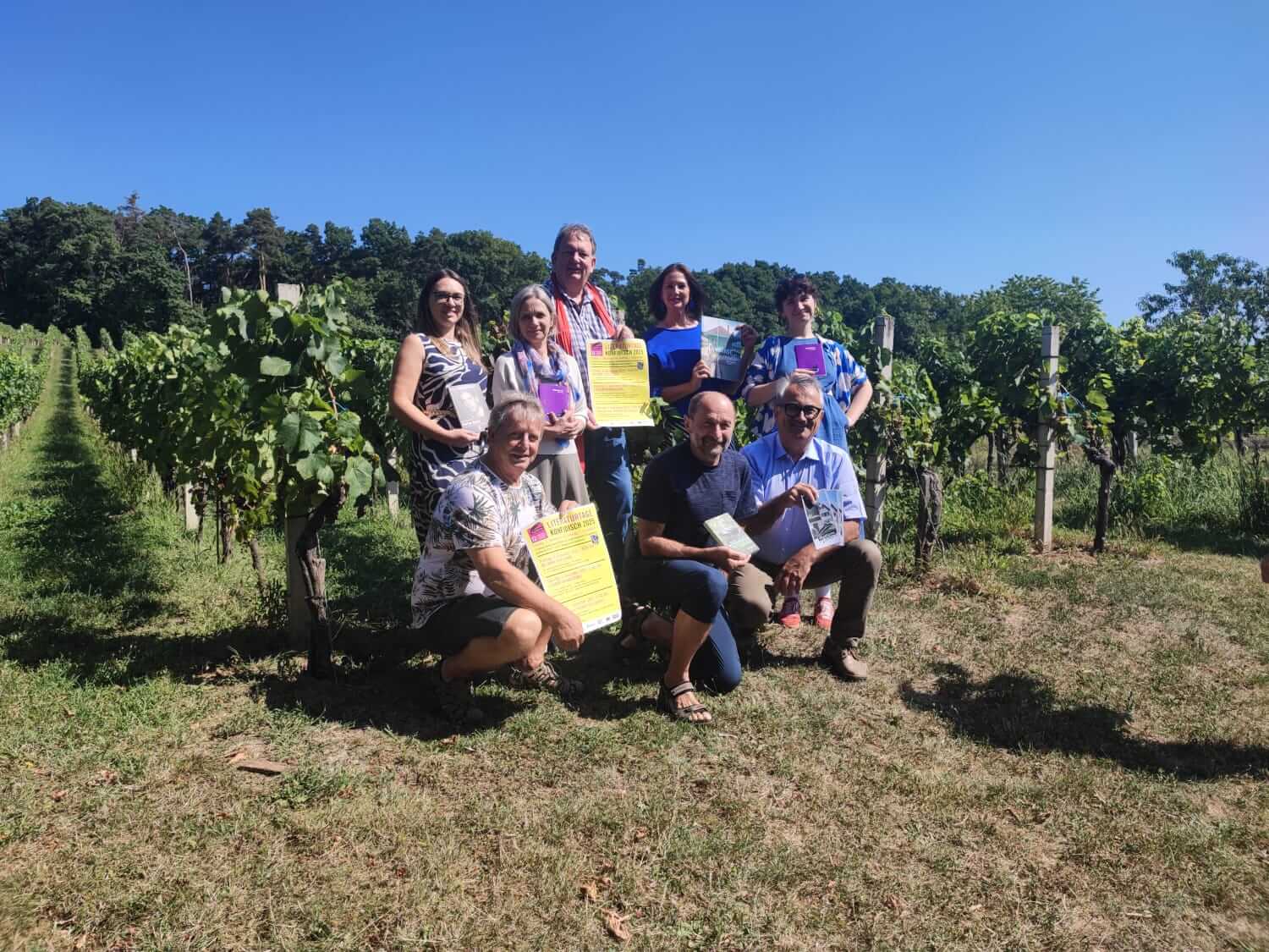Menschen bei sonnigem Tag im Weinberg mit Prospekten, Blätter und Reben im Hintergrund.