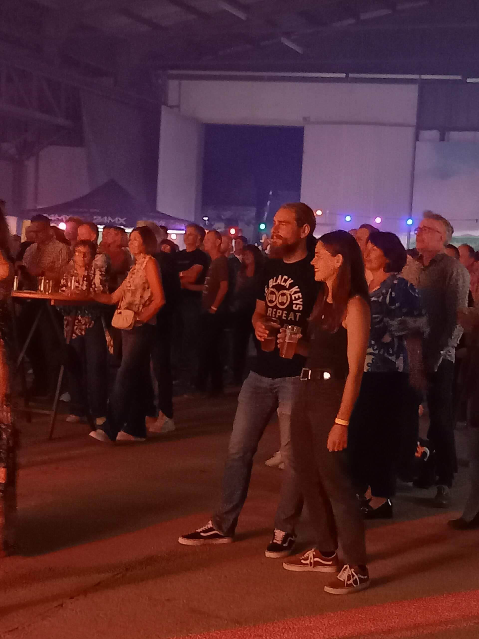 Menschen genießen ein Konzert in einer belebten Halle mit buntem Licht für ein entspanntes Eventerlebnis.