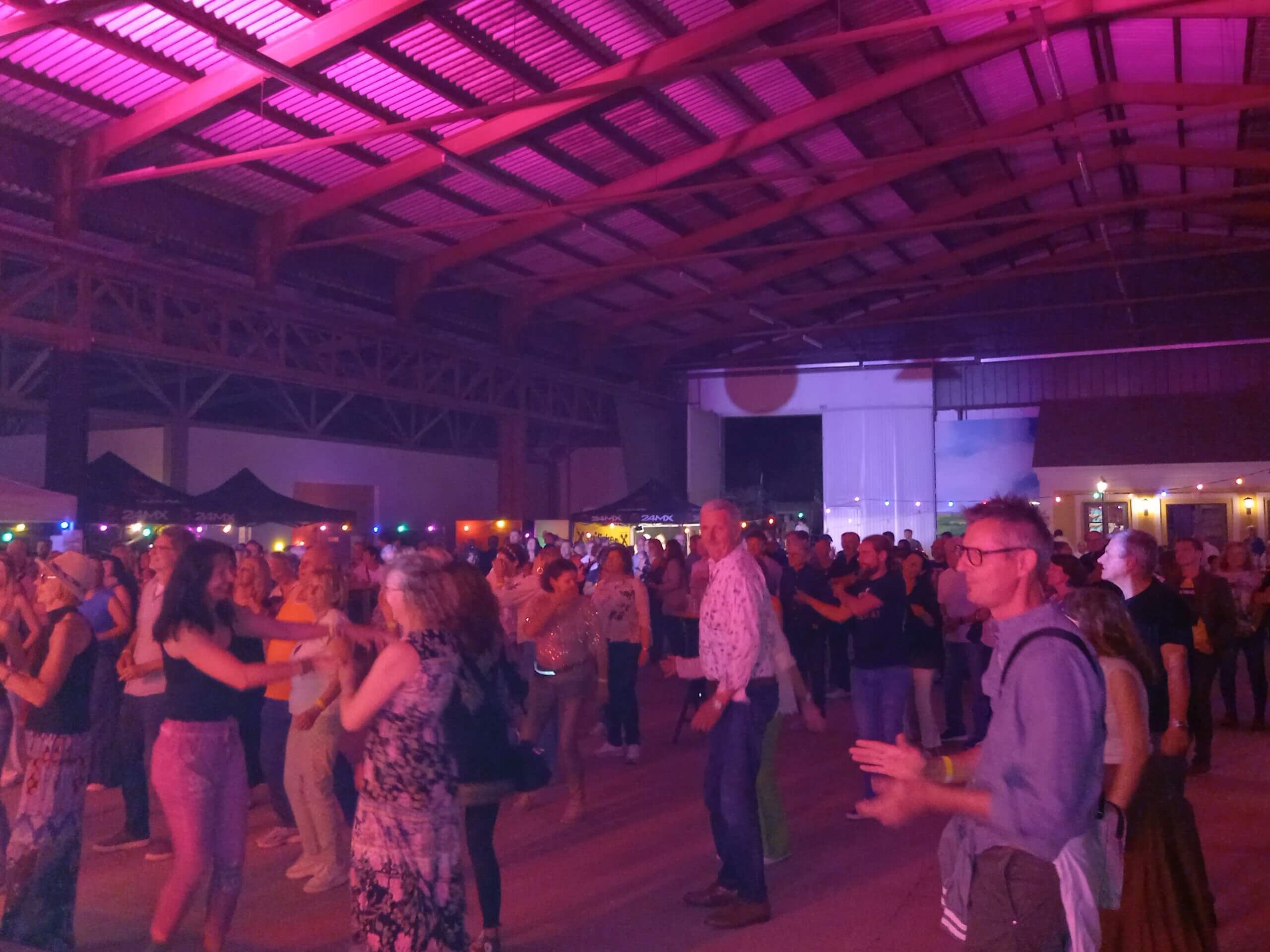 Menschen tanzen und feiern auf einer Party in einer bunt beleuchteten Halle mit hoher Decke.