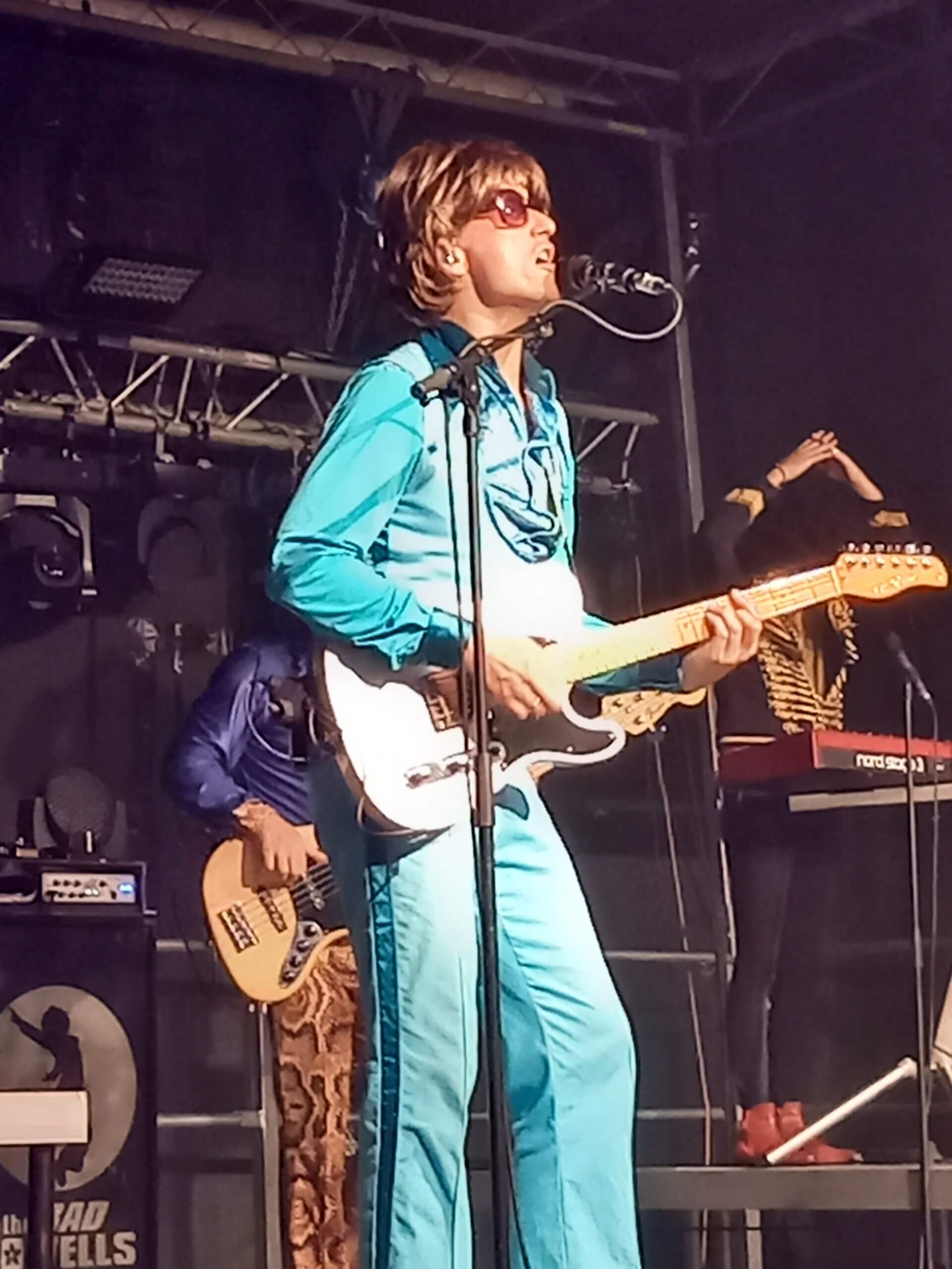 Musiker in blauem Anzug mit Gitarre auf Konzertbühne, unterhaltsame Live-Performance voller Energie.