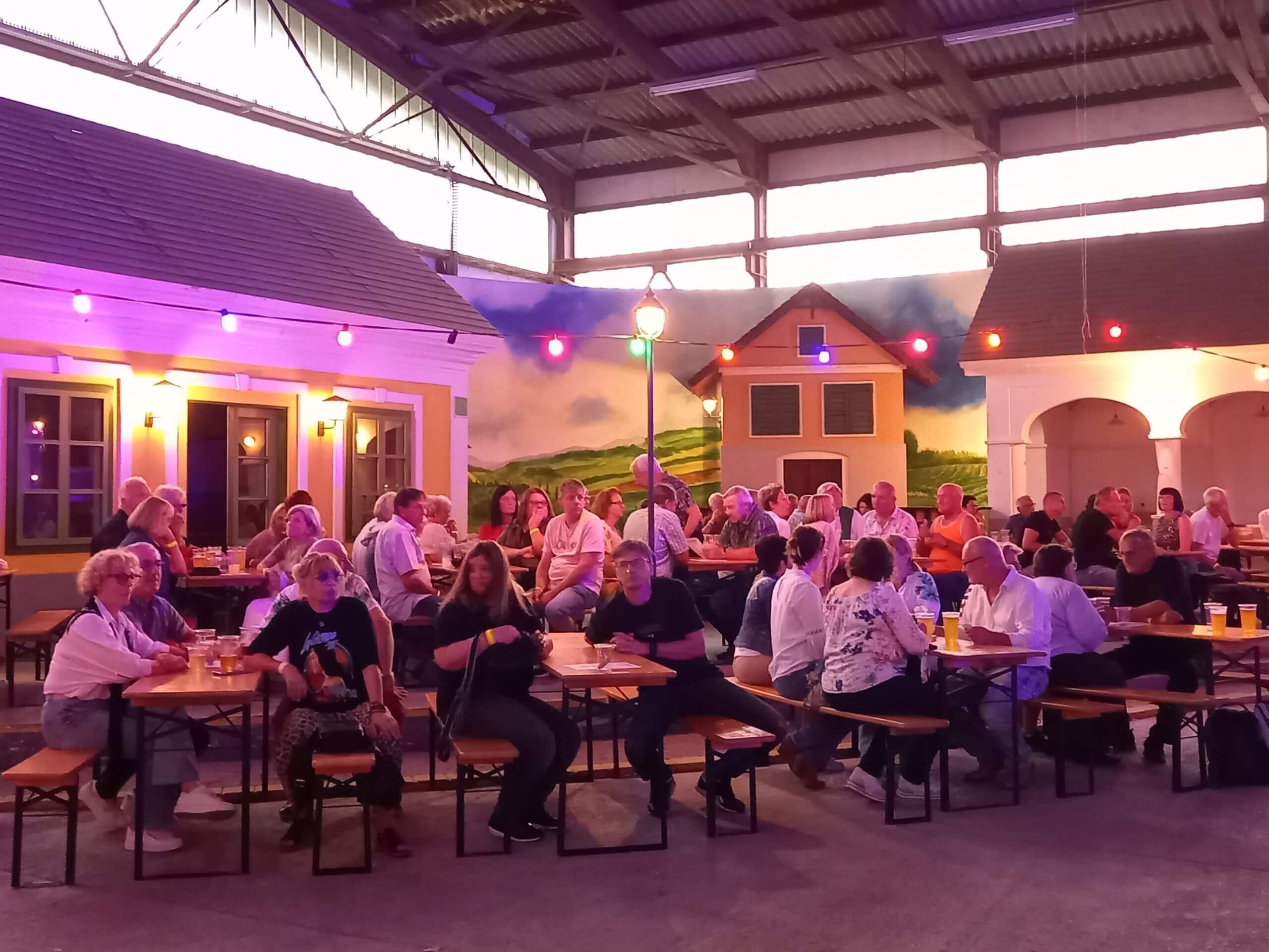 Menschen genießen abendliches Beisammensein in einer bunt beleuchteten Biergartenatmosphäre unter einem Pavillon.