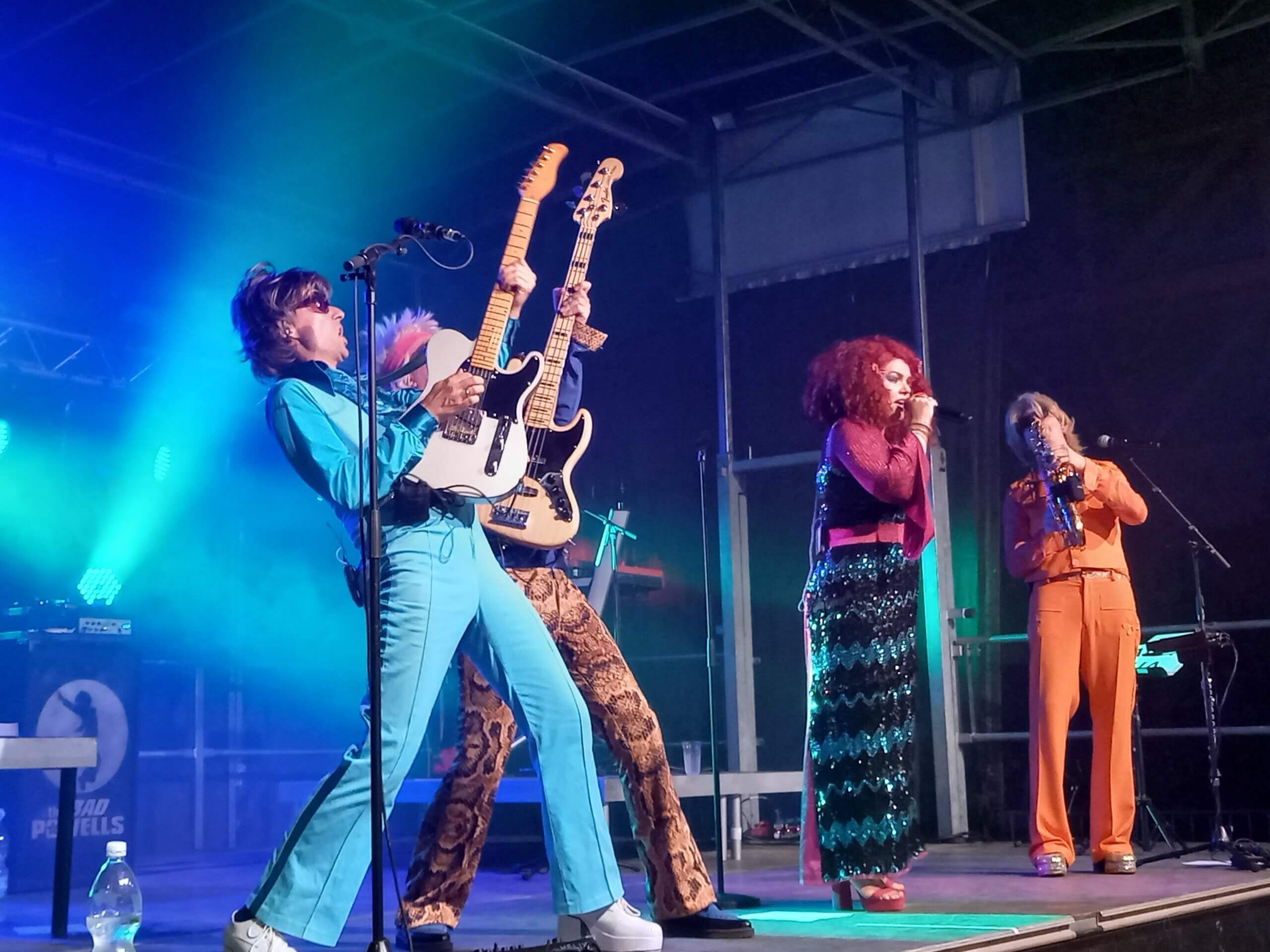 Band performt live auf einer Bühne, mit energiegeladenen Musikern und buntem Licht, schafft Festivalstimmung.