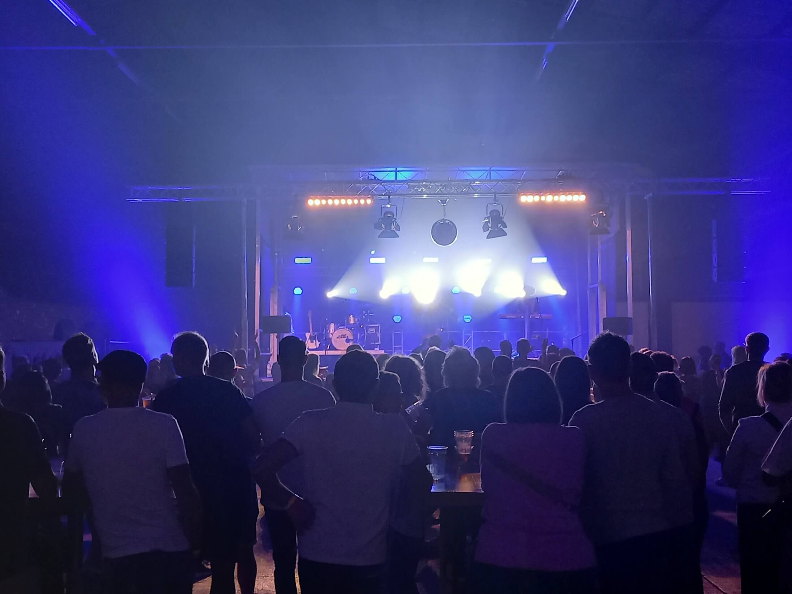 Konzertbesucher genießen eine Live-Show mit atmosphärischer Beleuchtung und Bühne voller Instrumente.