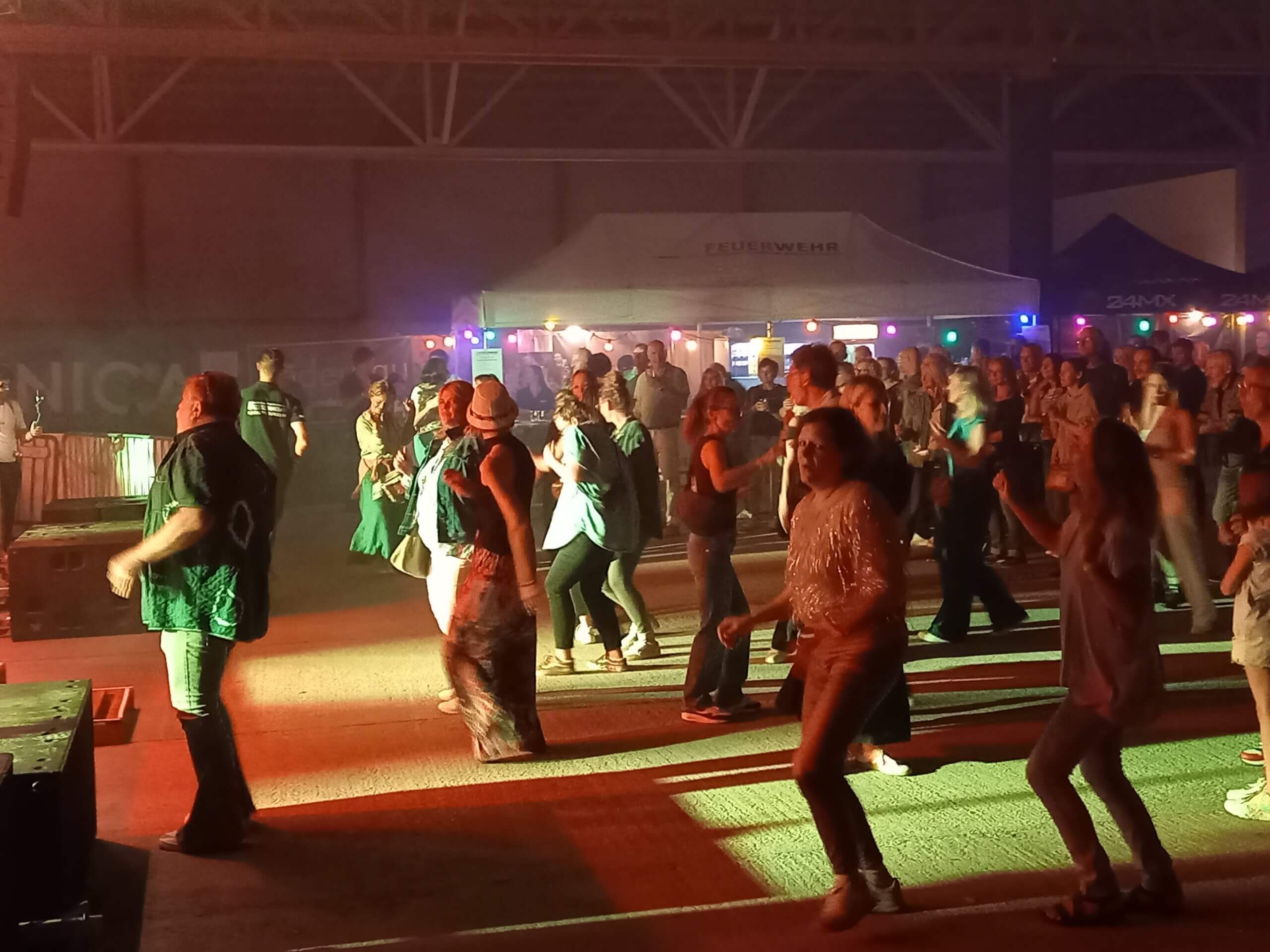 Menschen tanzen fröhlich bei einem beleuchteten Indoor-Event mit Musik und entspannter Atmosphäre.