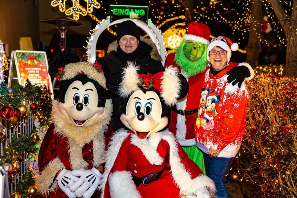 Gruppe posiert in weihnachtlichen Kostümen mit Micky und Minnie Maus bei festlichen Lichtern.