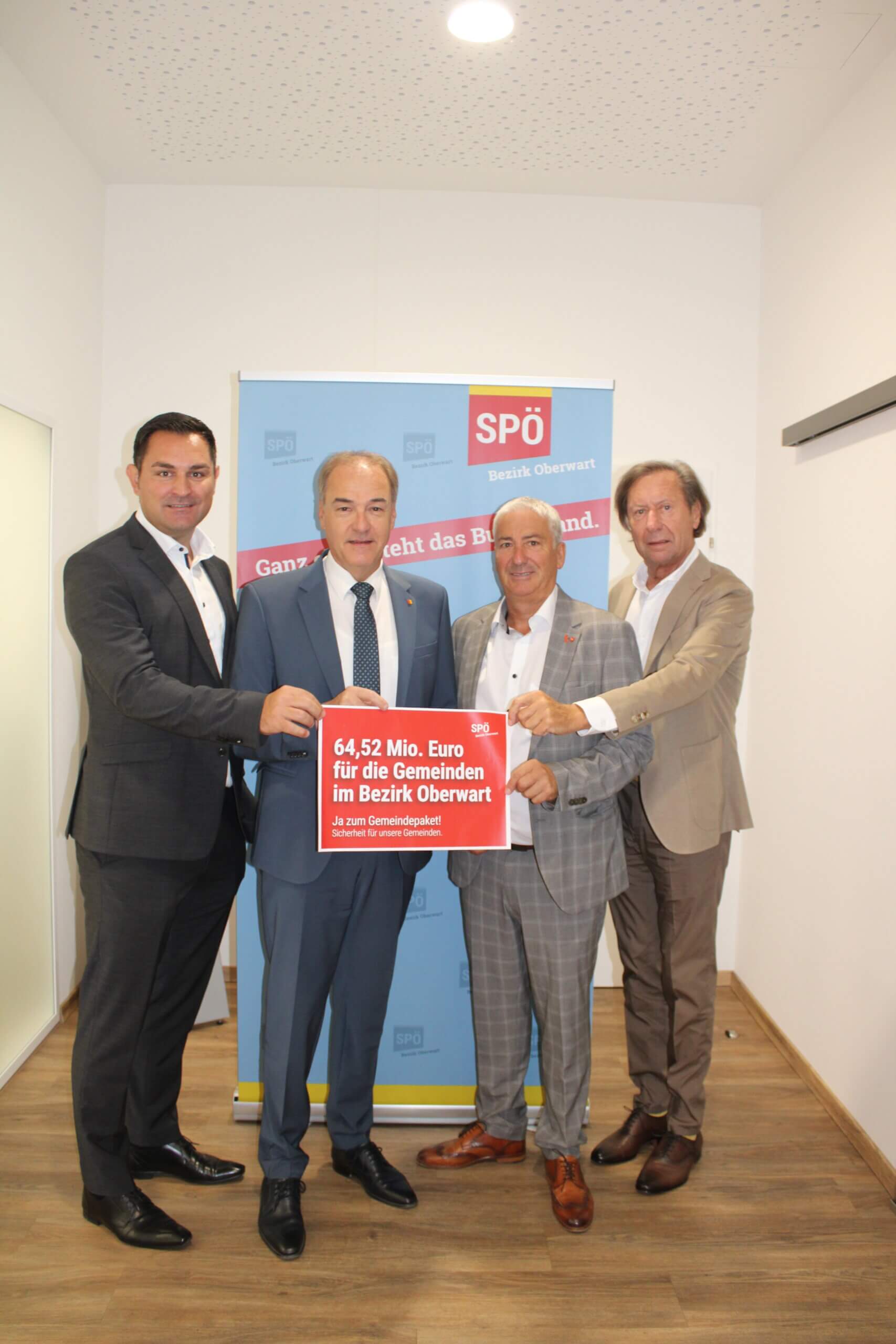Männer präsentieren Schild für 64,52 Mio. Euro Fördermittel im Bezirk Oberwart, SPÖ-Event, Gruppenfoto im Büro.