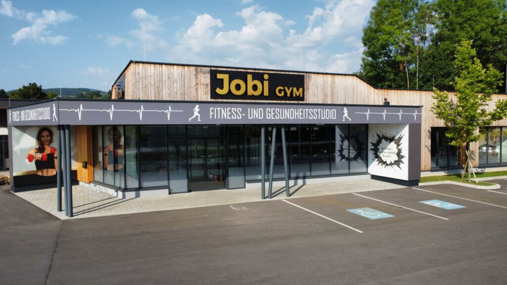 Außenansicht des Jobi Gym Fitness- und Gesundheitsstudios mit moderner Architektur und freien Parkplätzen.
