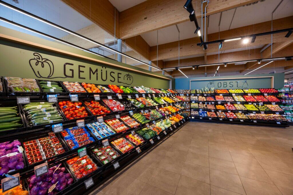 Supermarktabteilung mit frischem Gemüse und Obst, gut beleuchtet und organisiert in Regalen.