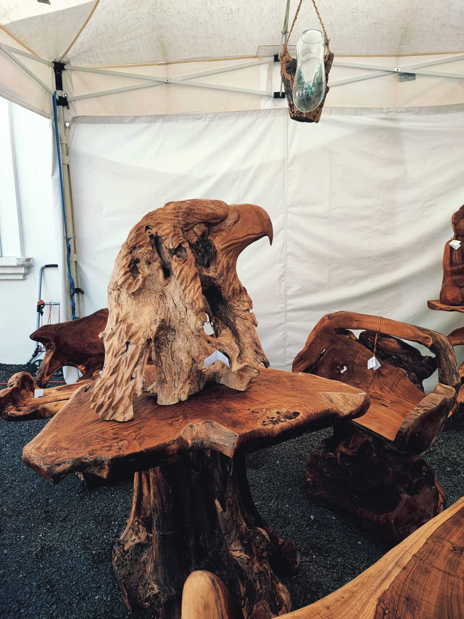 Holztisch und Stühle mit kunstvollen Adler-Schnitzereien auf einer Ausstellung unter einem weißen Zelt.