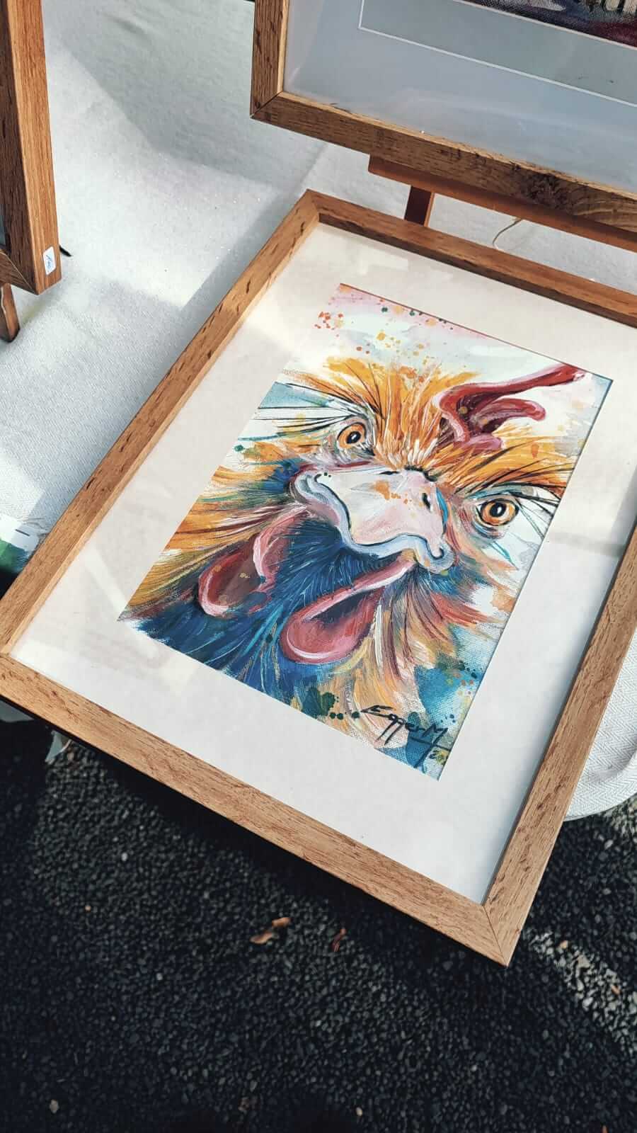 Gerahmtes, buntes Hühnerbild in Aquarelltechnik auf Kunstmarkt. Farbenfrohe Kunst, Holzrahmen, lebendiger Eindruck.