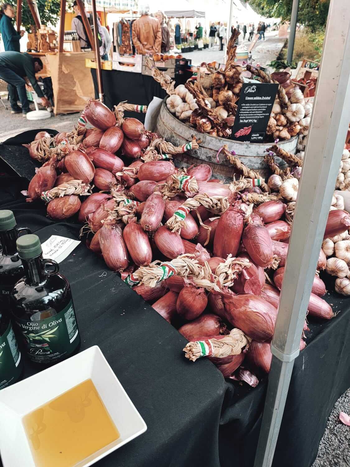 Frischer Marktstand mit roten Zwiebeln, Knoblauch und Olivenöl in rustikaler Umgebung. Ideal für Feinschmecker.