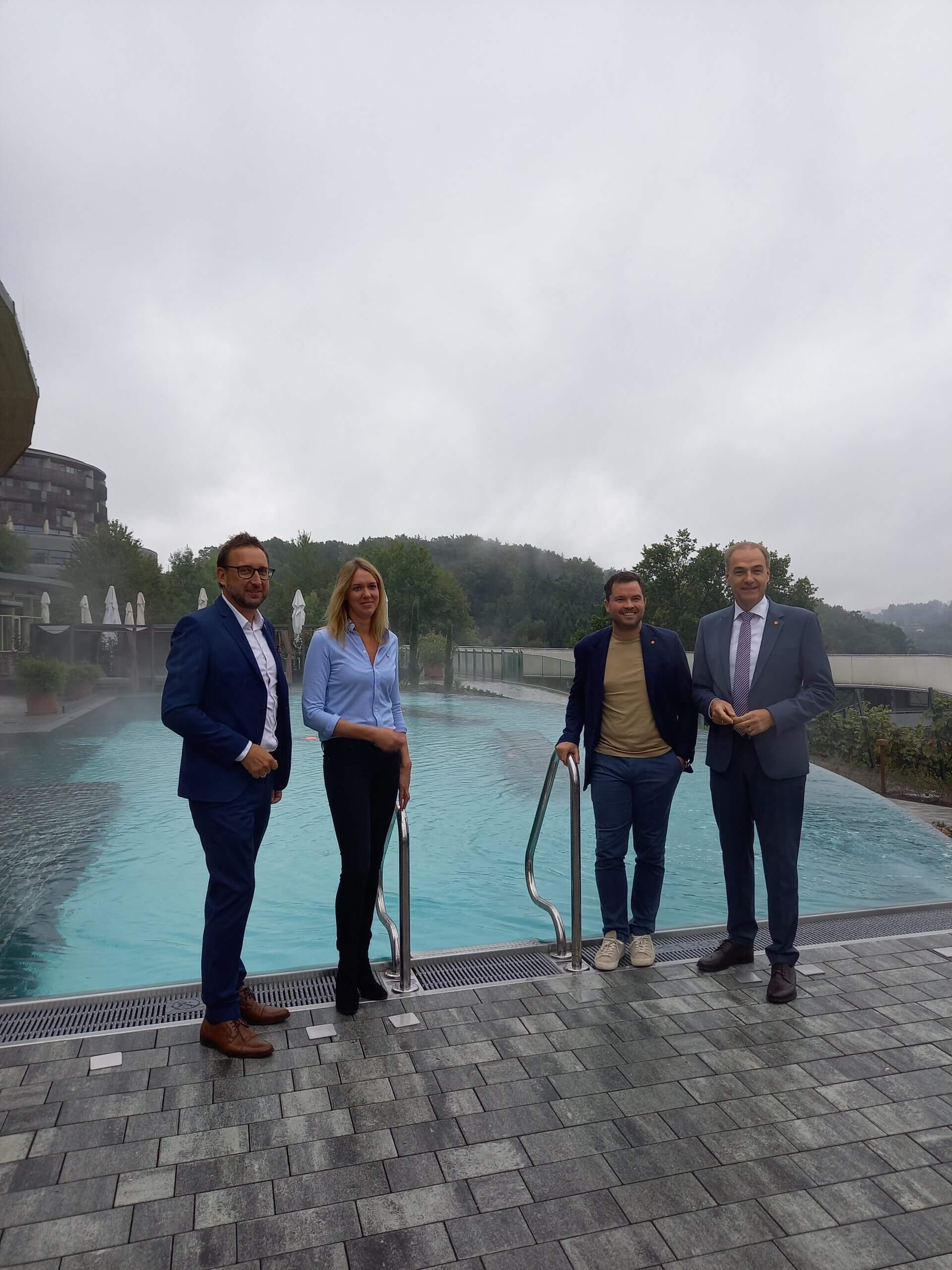 Vier Personen stehen bei bewölktem Himmel neben einem Pool im Freien.