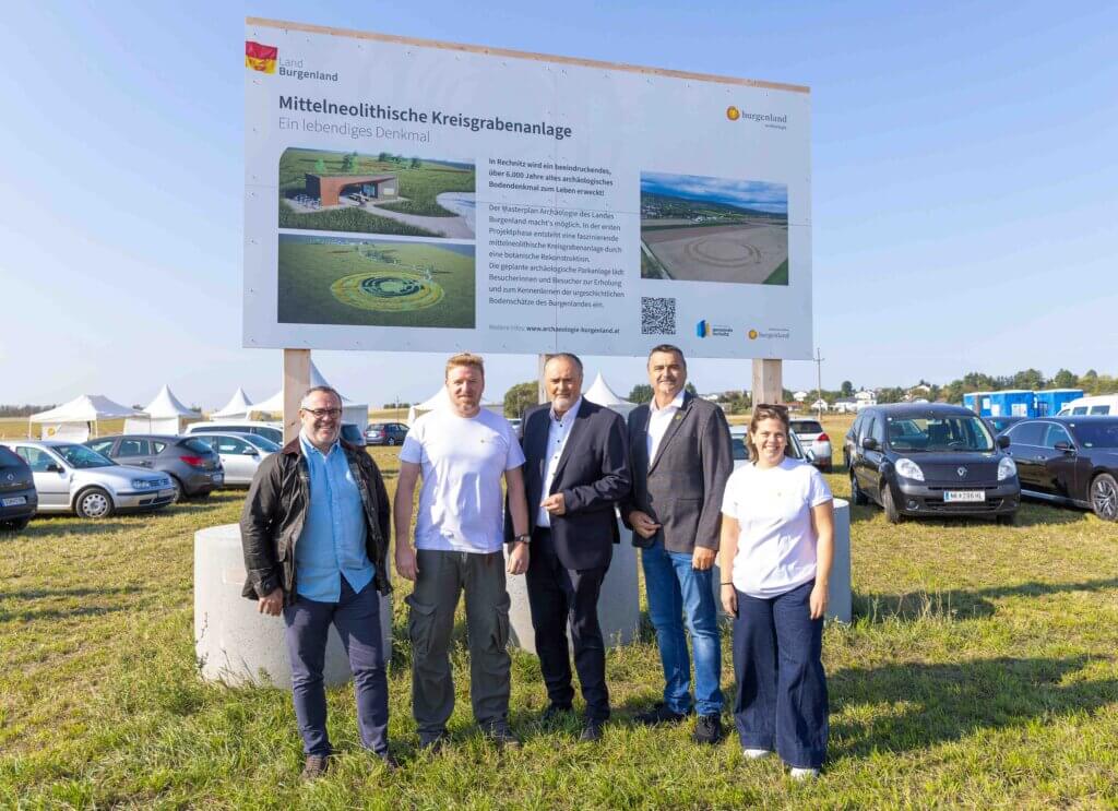 Gruppe vor Infotafel zur mittelneolithischen Kreisgrabenanlage in Burgenland, Österreich, bei sonnigem Wetter.