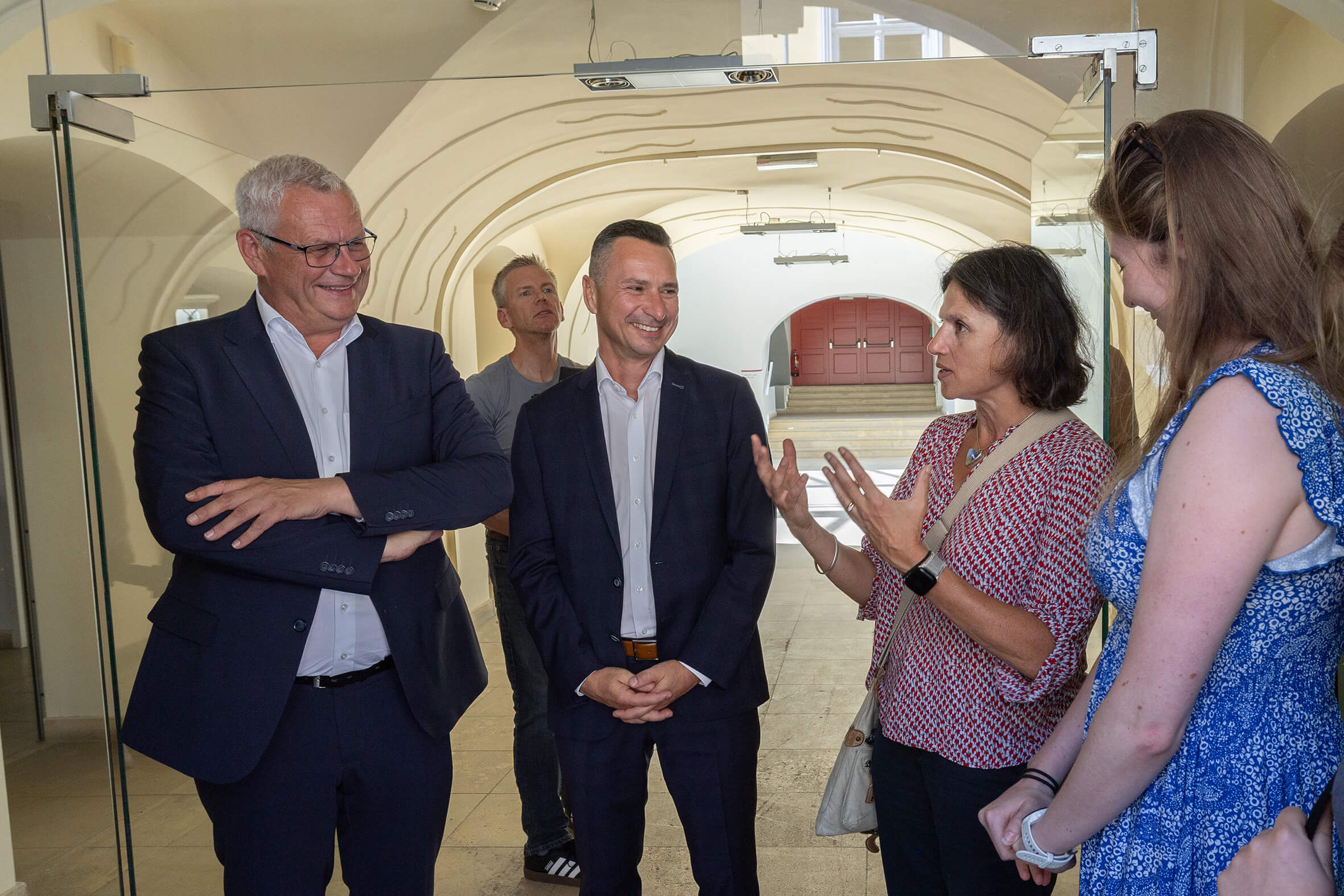 Gruppe diskutiert in modernem gläsernen Eingangsbereich eines Gebäudes, stilvolle Architektur im Hintergrund.